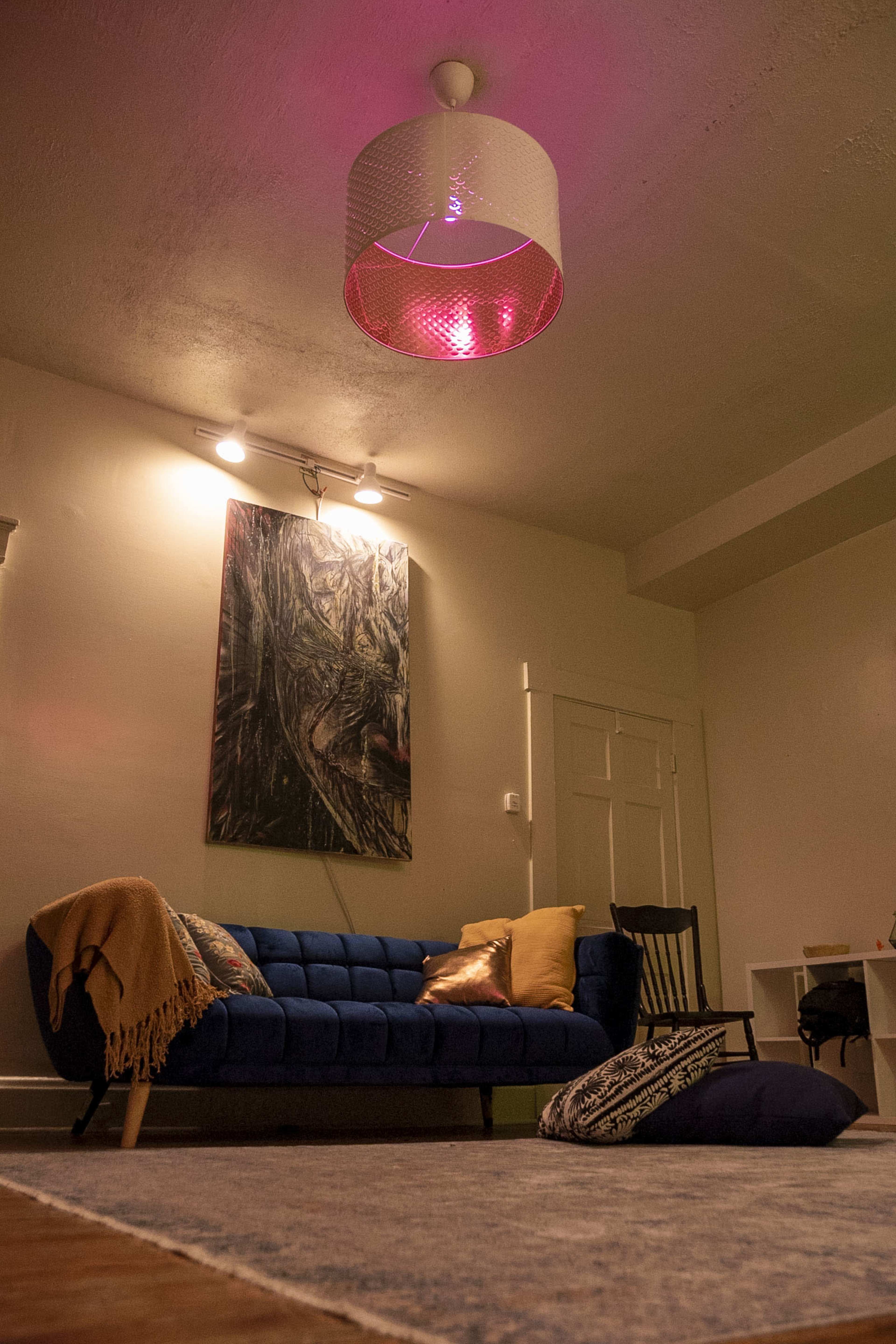 A living room features a blue sofa, a patterned rug, a black rocking chair, and a ceiling light with a decorative shade.