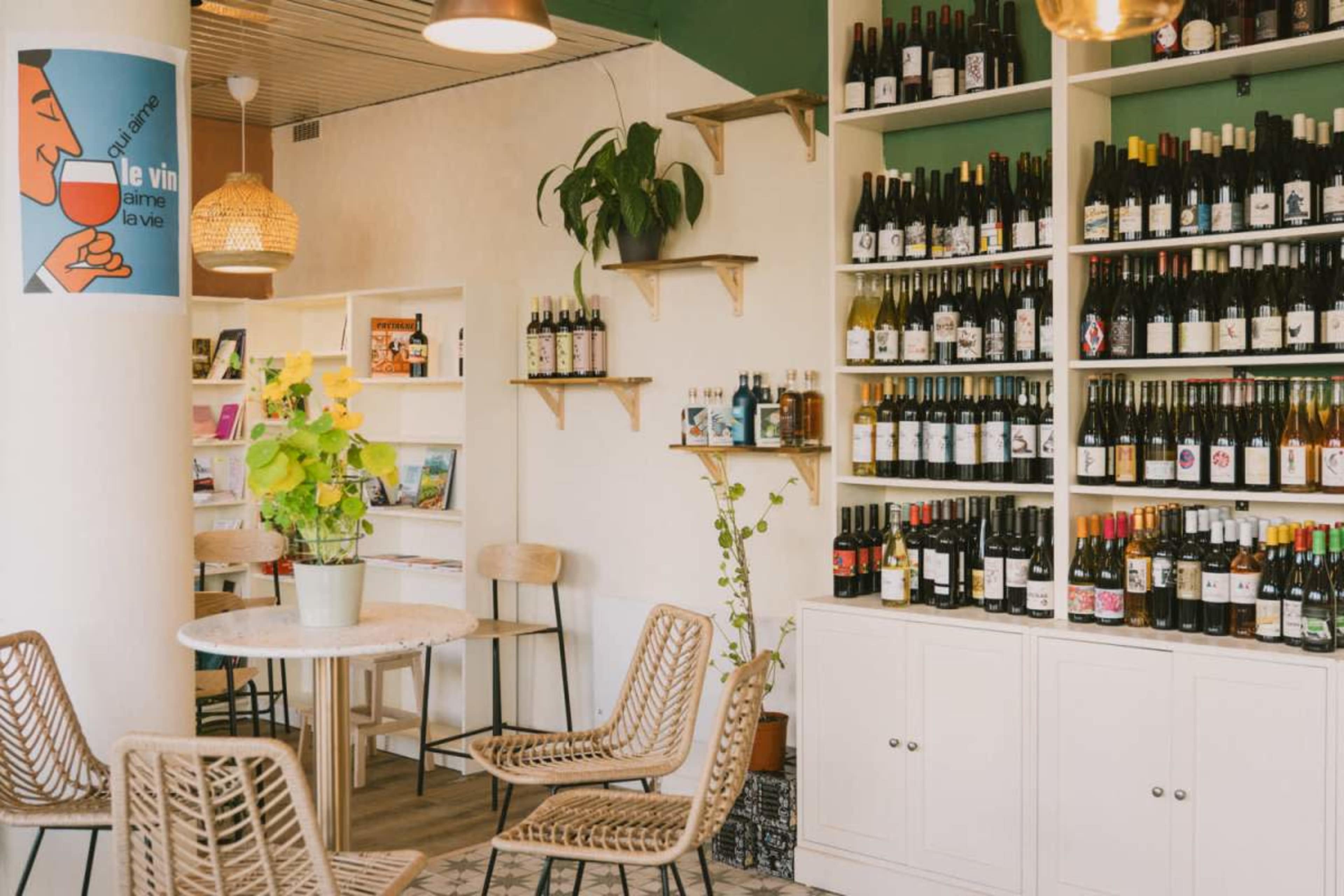 The image shows a cozy interior of a wine shop, featuring wooden shelves lined with various bottles of wine and a few seating arrangements.
