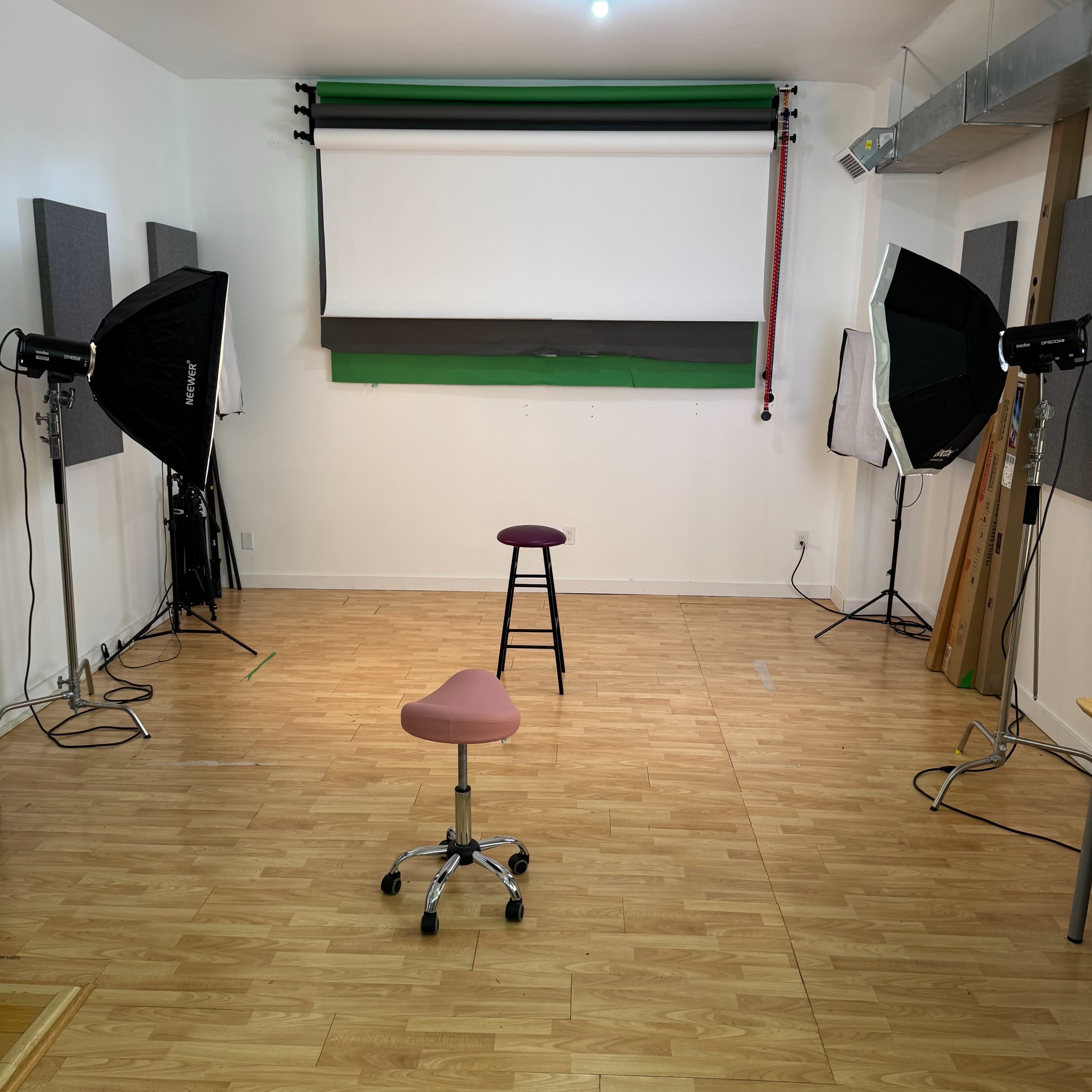 The image shows a studio space with two chairs and several lighting setups surrounded by soundproof panels.