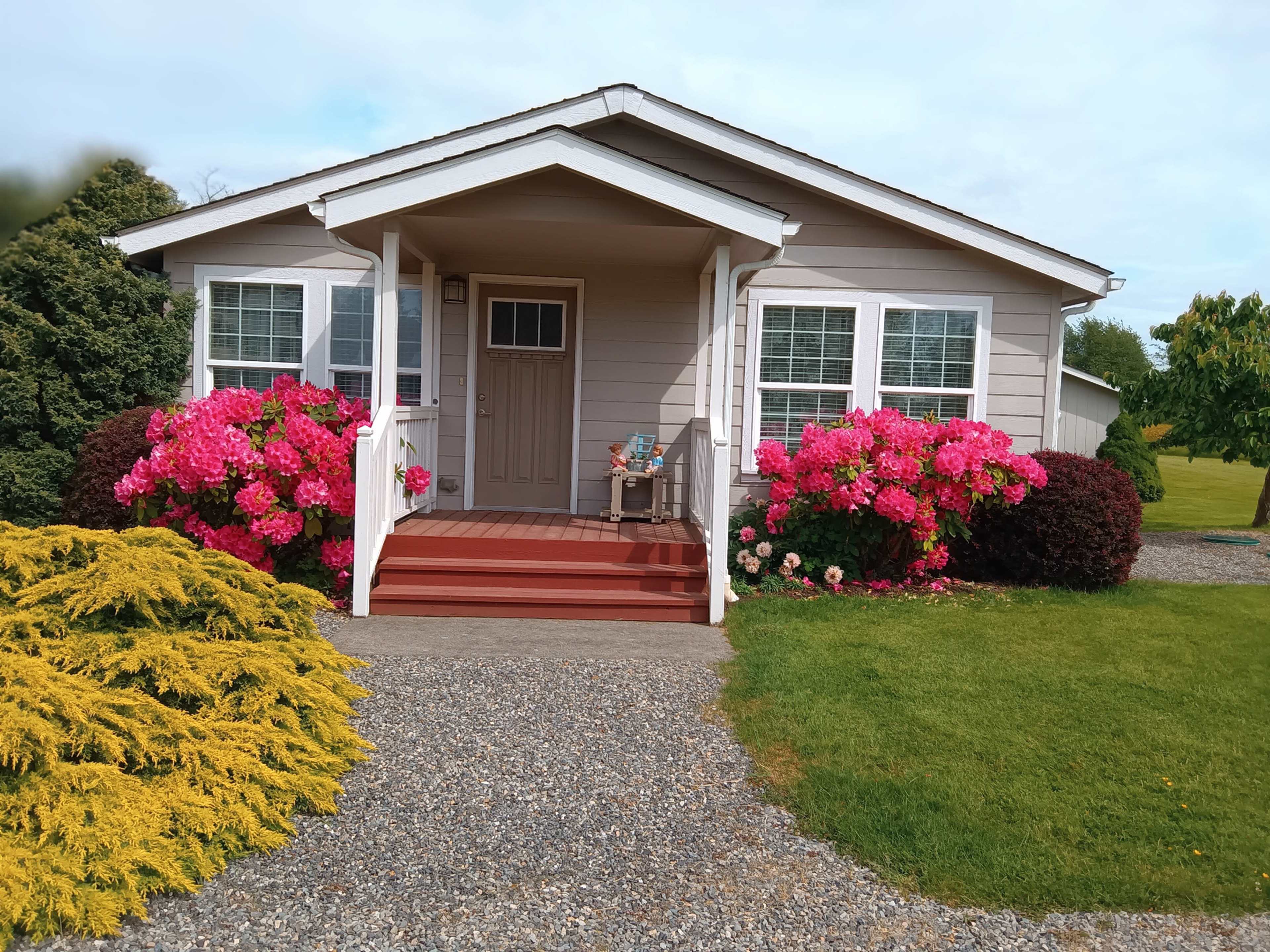 A house with a front porch is surrounded by vibrant pink flowers and neatly landscaped greenery.