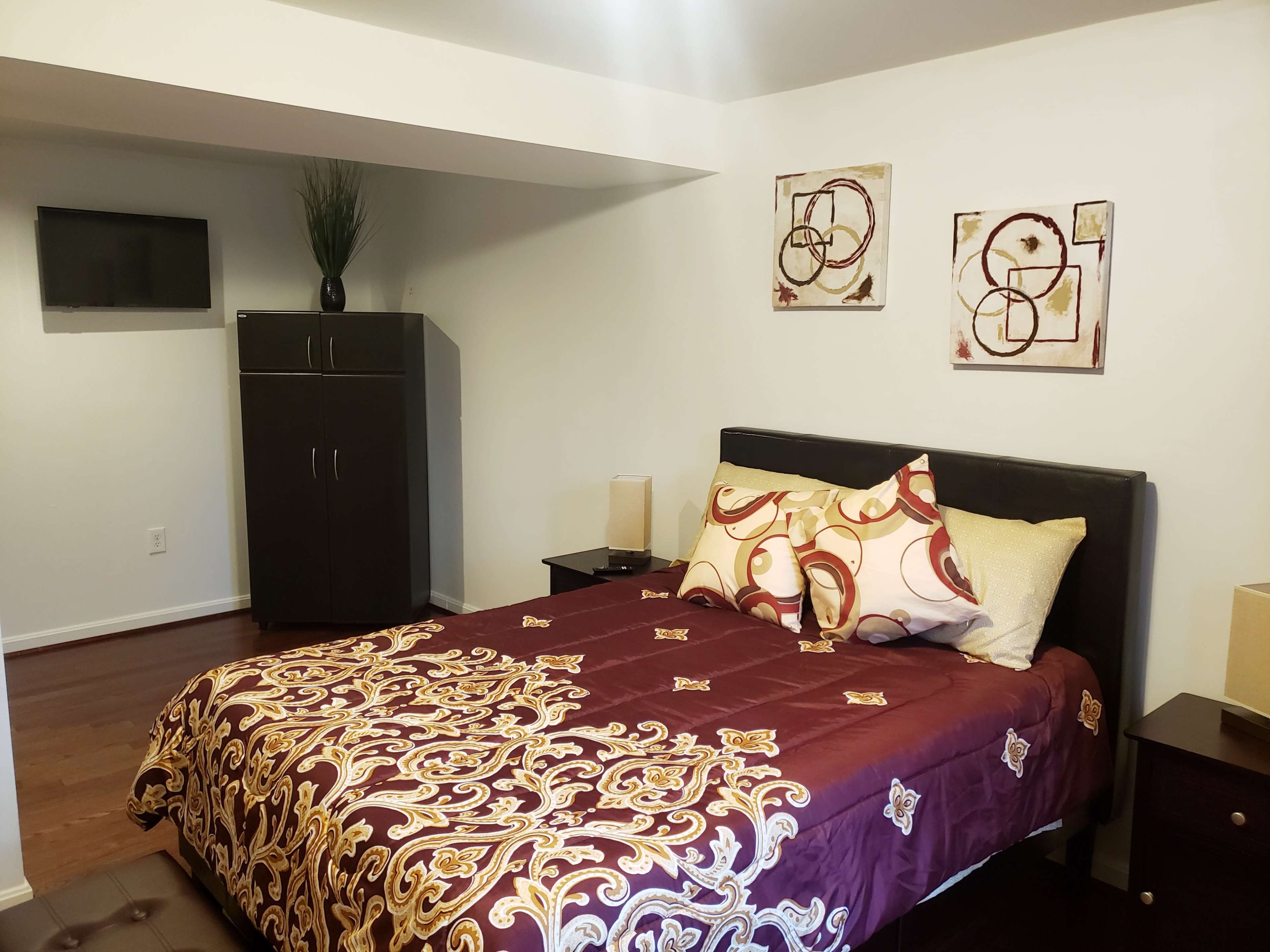 A bedroom with a queen-sized bed, two nightstands, a dresser, and a small television mounted on the wall.