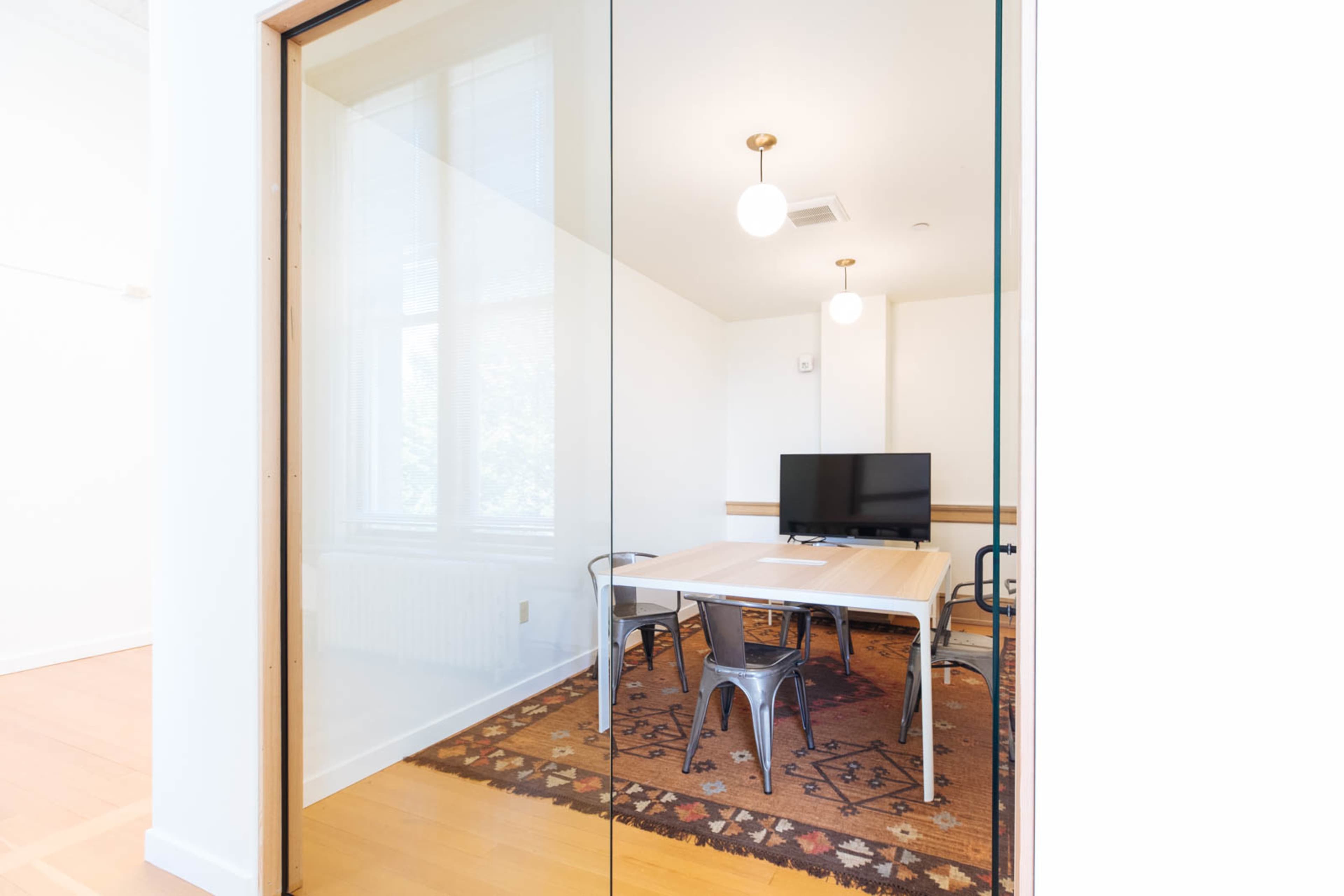 A conference room features a wooden table surrounded by metal chairs and a television on the wall.
