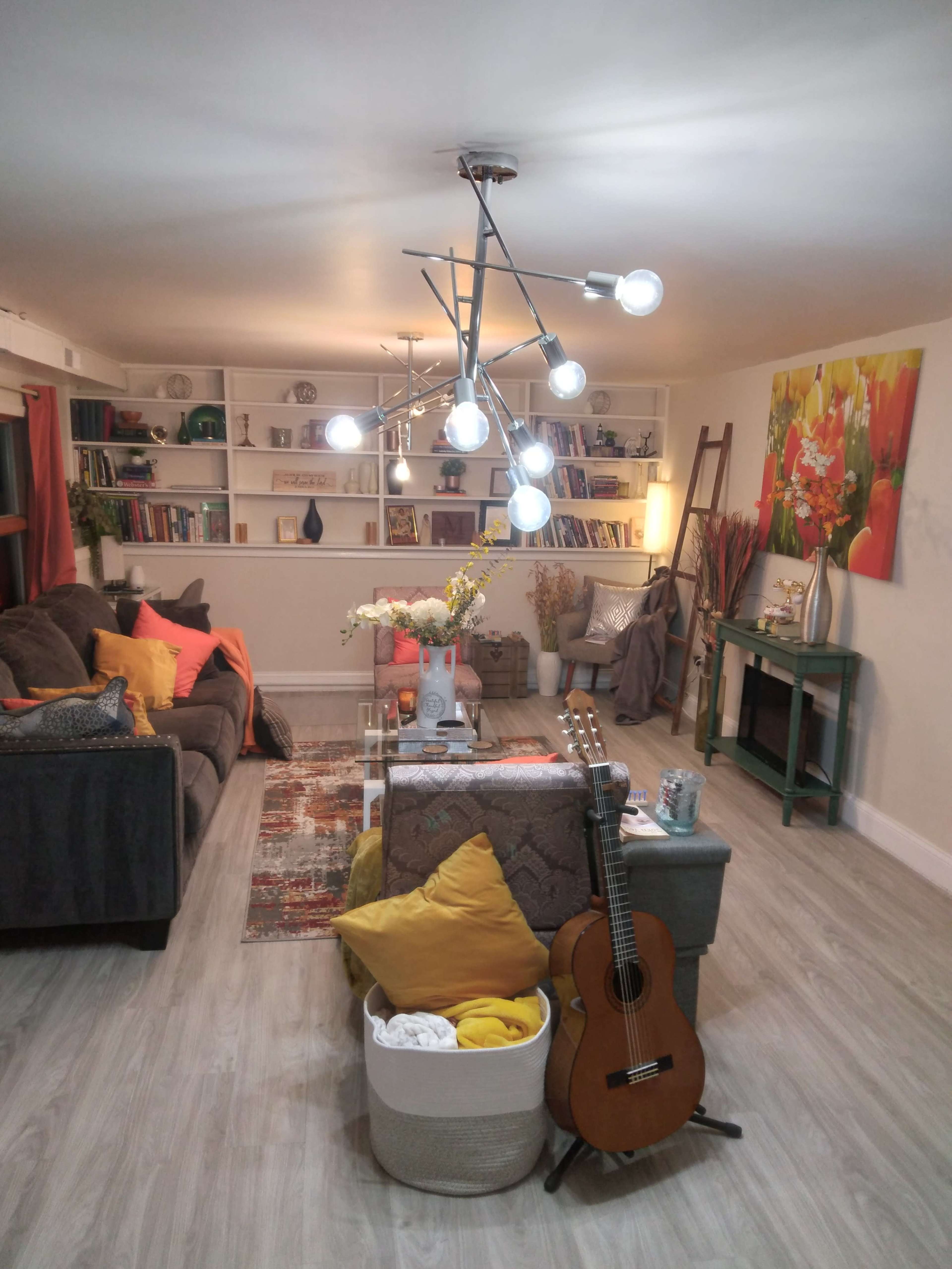 A cozy living room with a gray sofa, colorful cushions, a coffee table, a guitar, and a modern light fixture.