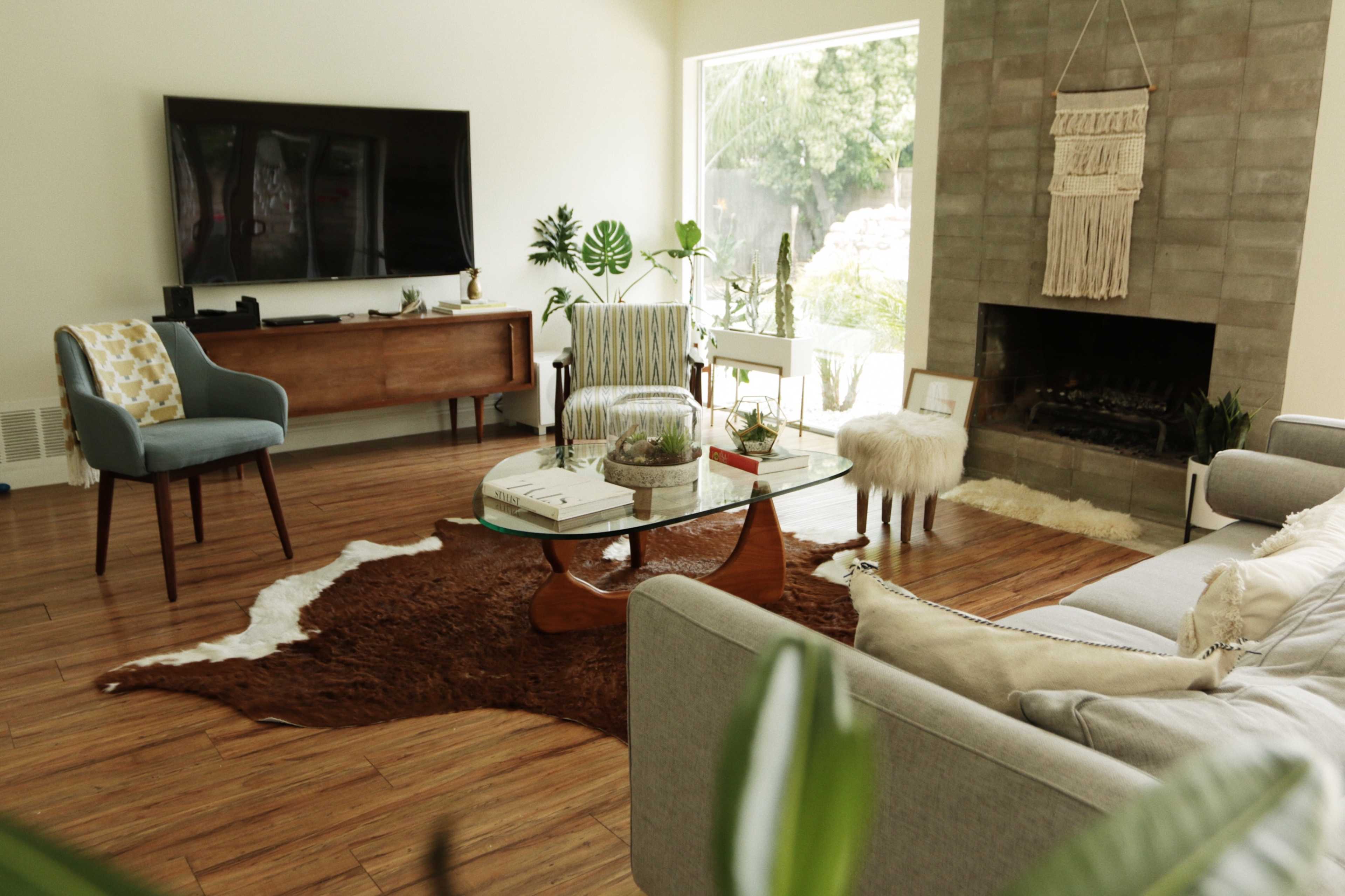 The living room features a gray sofa, a glass coffee table on a brown area rug, a wooden sideboard, and a stone fireplace with a decorative wall hanging.