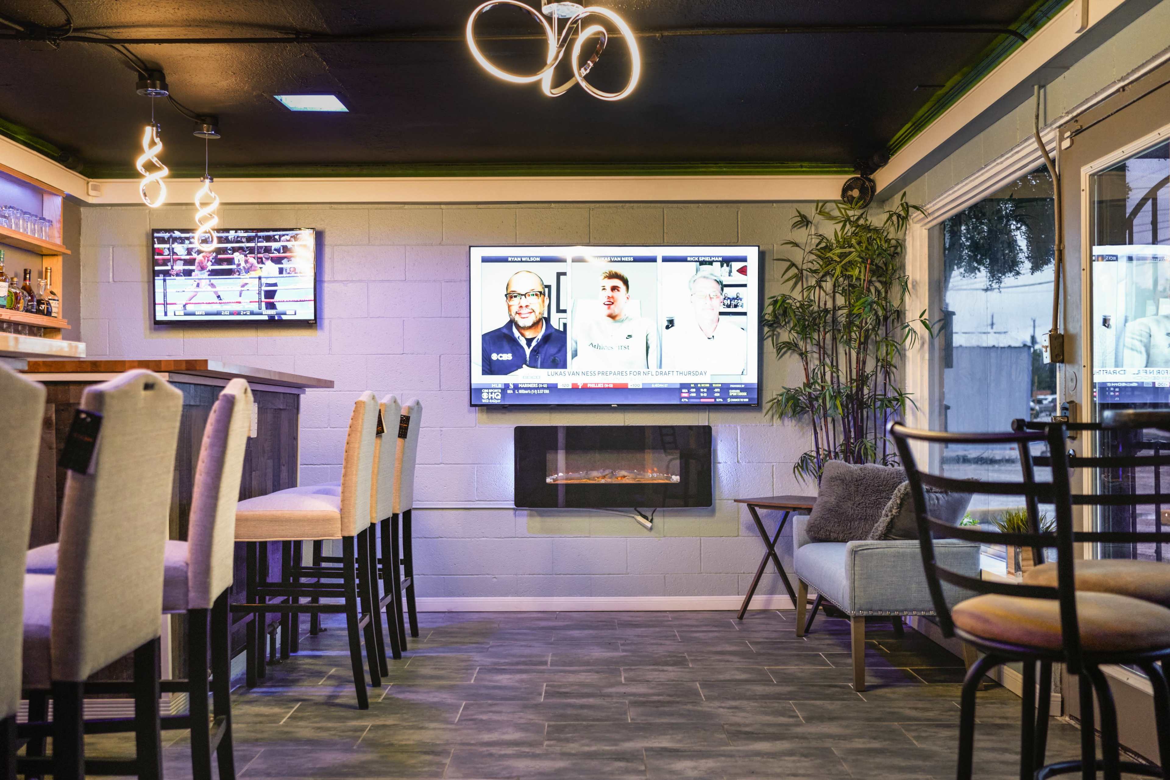 The image shows a modern bar area with a long counter, high stools, and multiple TVs displaying sports on the walls.