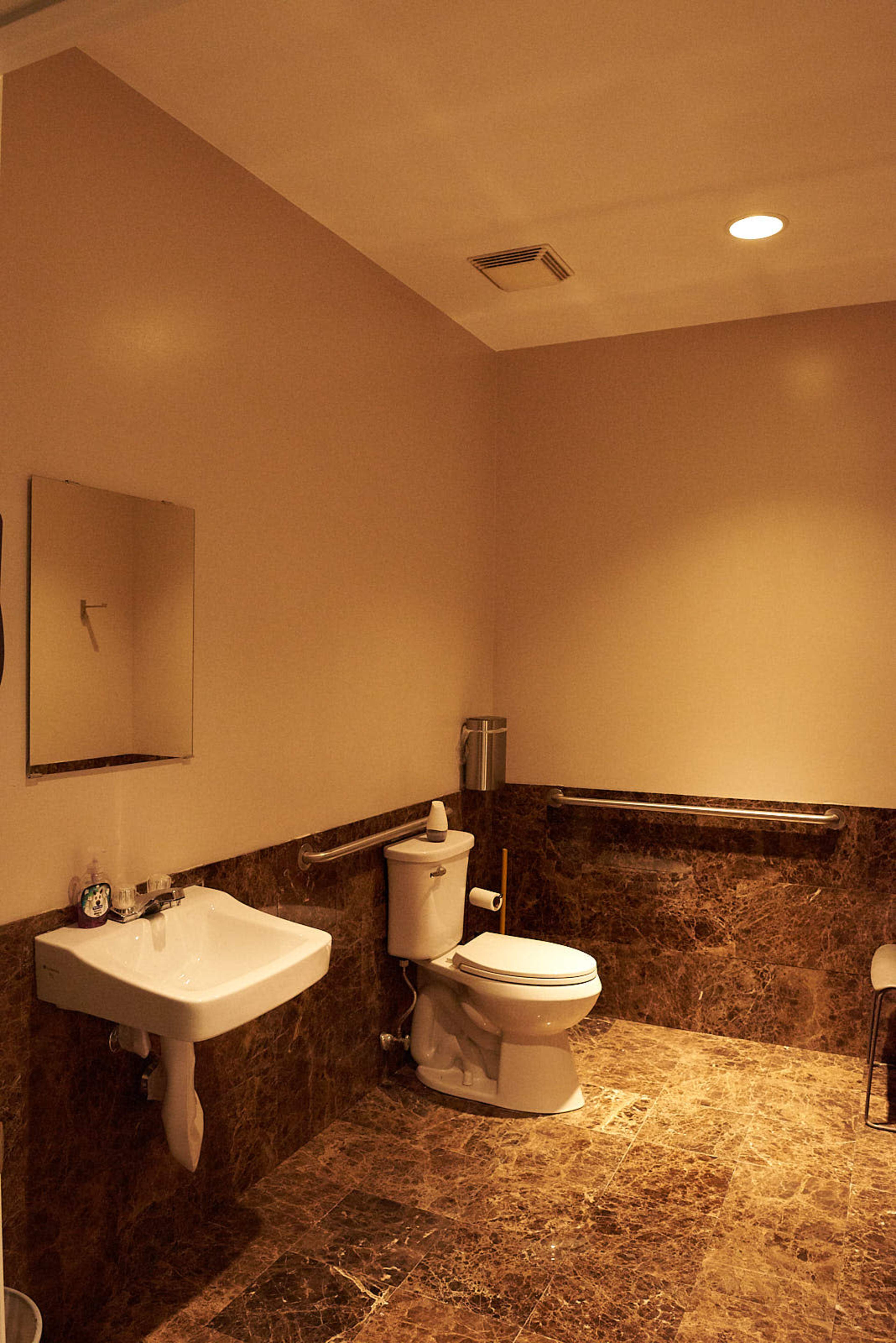 A bathroom with a toilet, a sink mounted on the wall, and marble-patterned flooring.