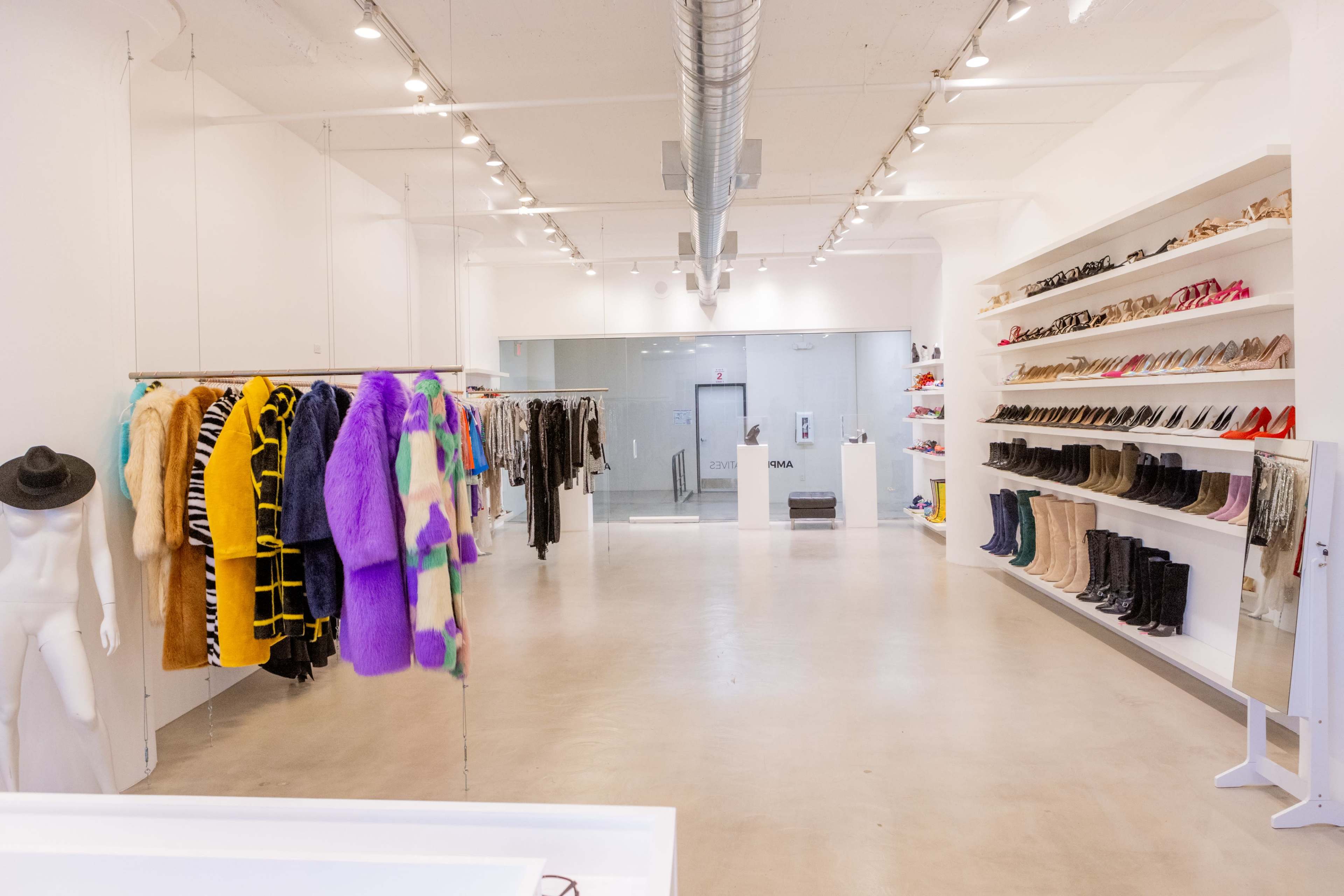 The image shows a spacious, modern clothing store with colorful garments hanging on racks and a variety of footwear displayed on shelves along the walls.