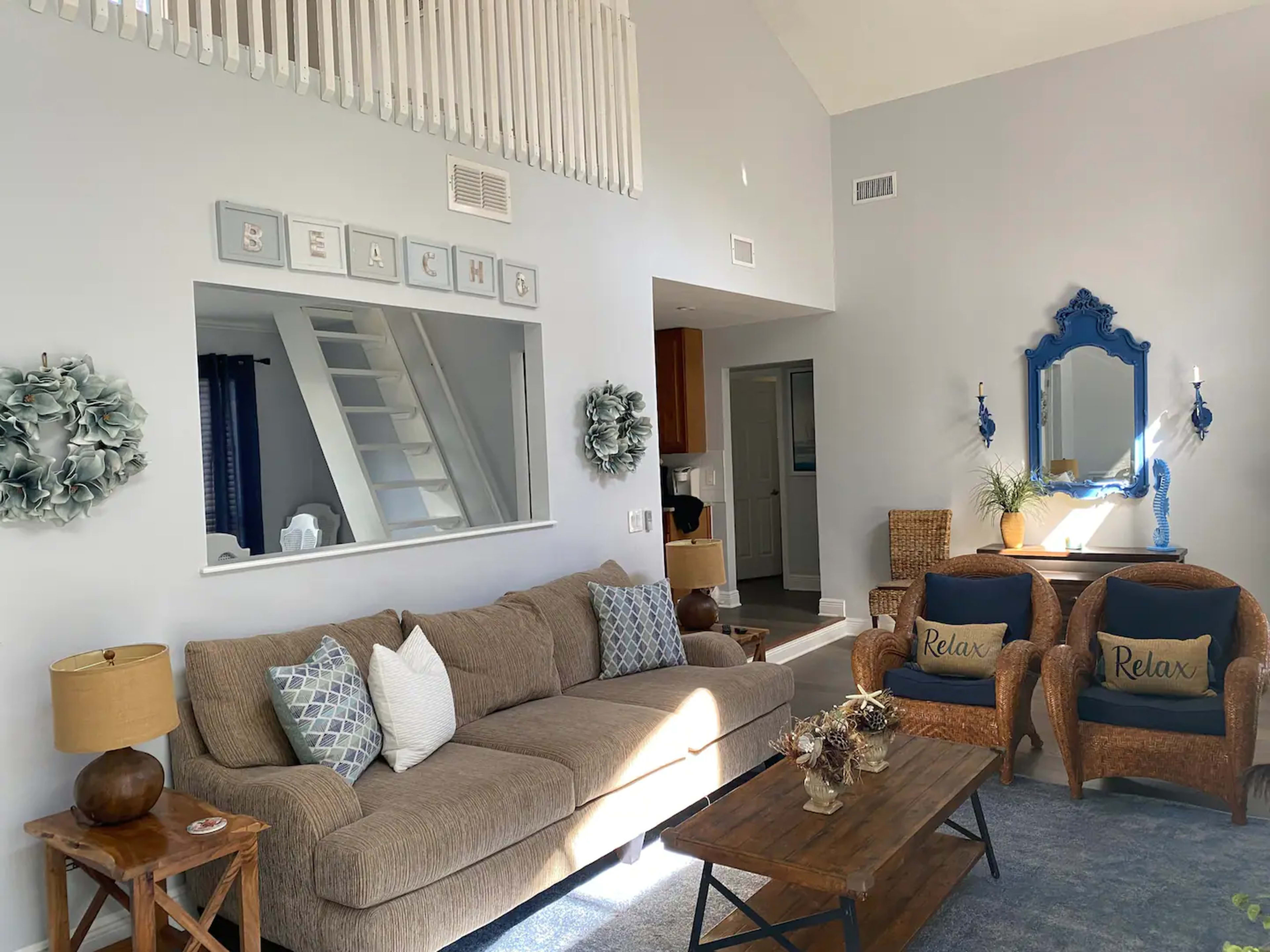 A spacious living room features a brown sofa, two blue accent chairs, a wooden coffee table, and a decorative mirror on the wall.