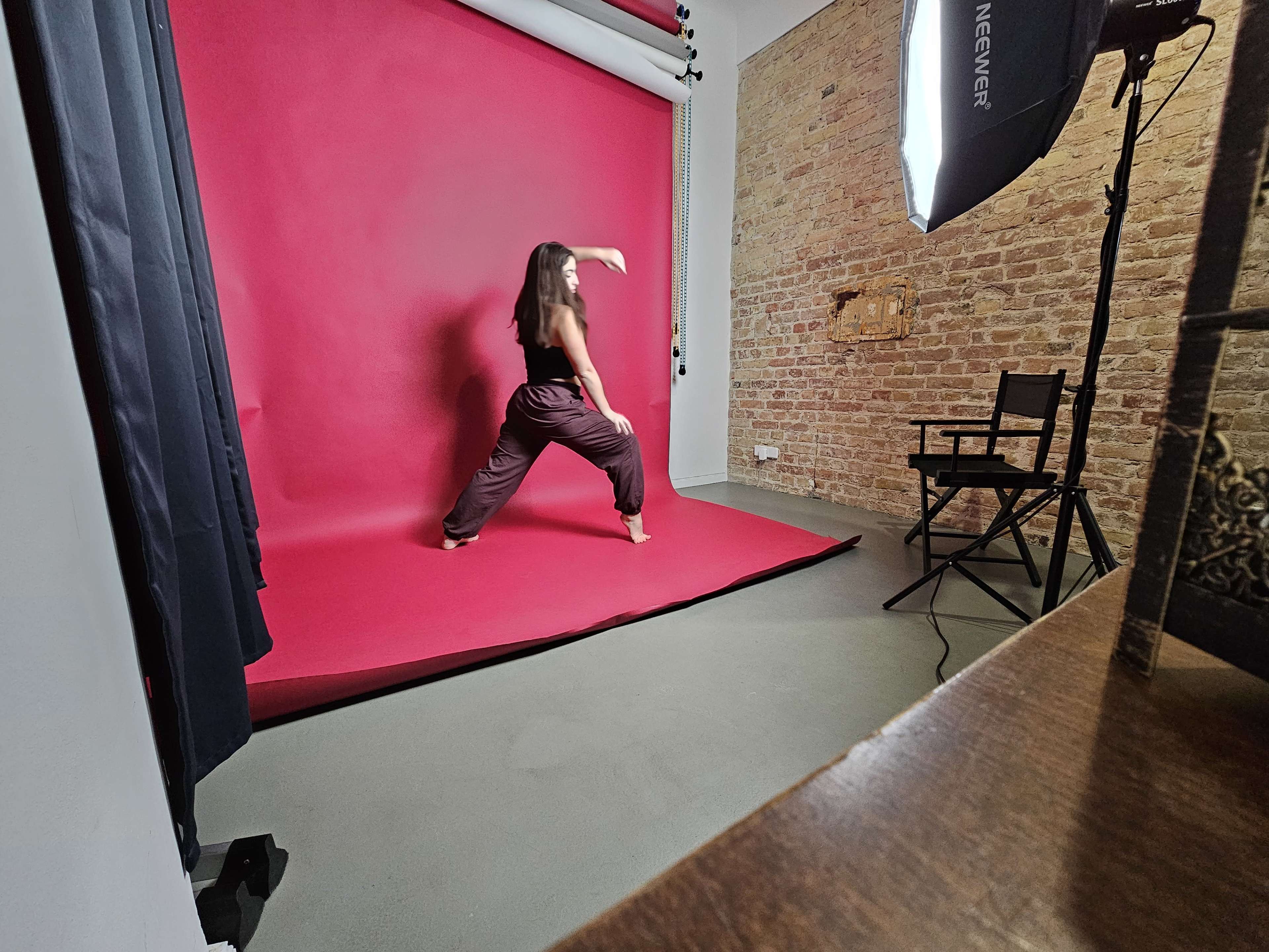 A dancer performs against a pink backdrop in a studio with exposed brick walls and a softbox light.