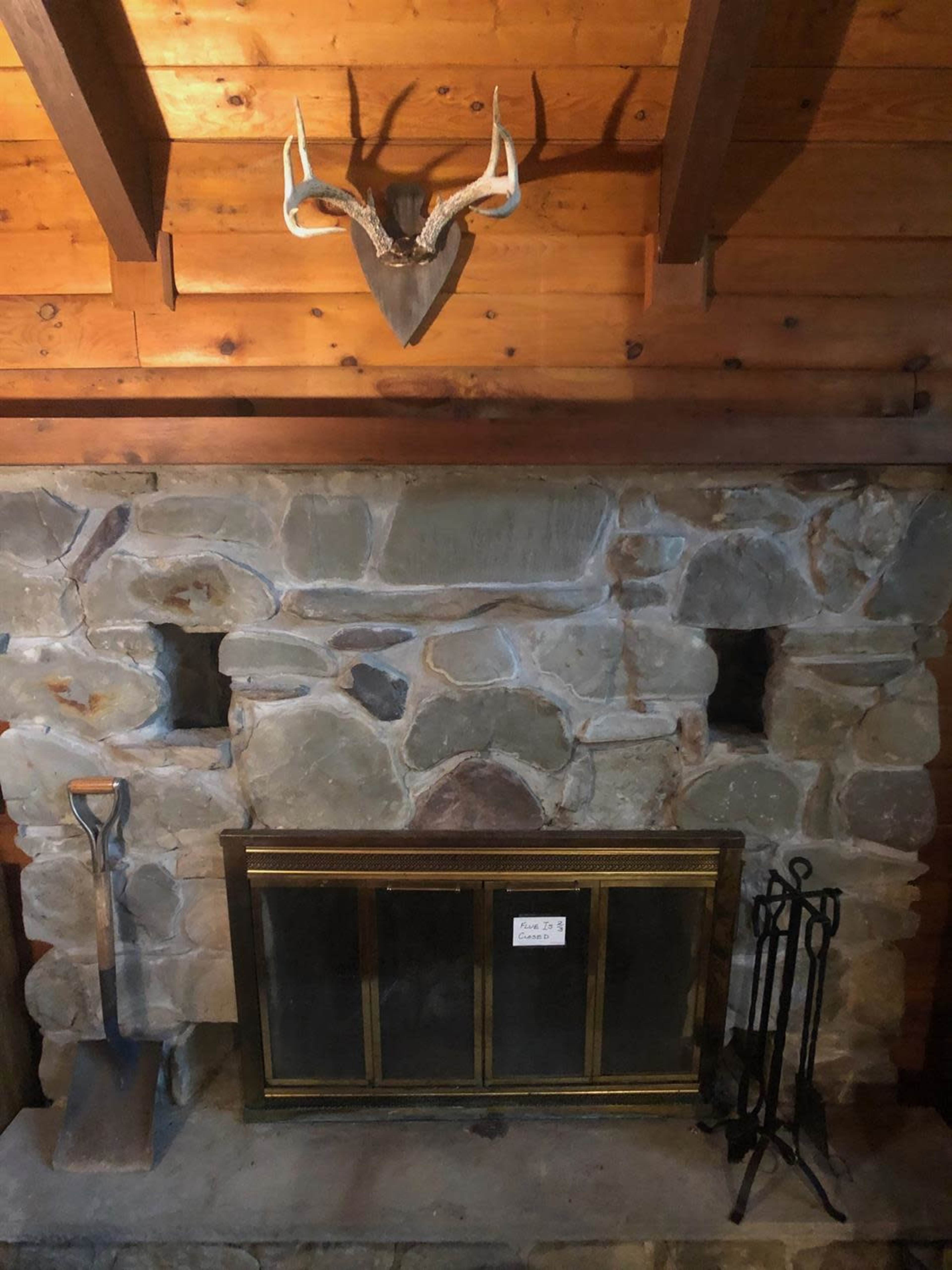 A stone fireplace with a metal grate, a shovel leaning against the side, and a decorative mounted deer head above it.