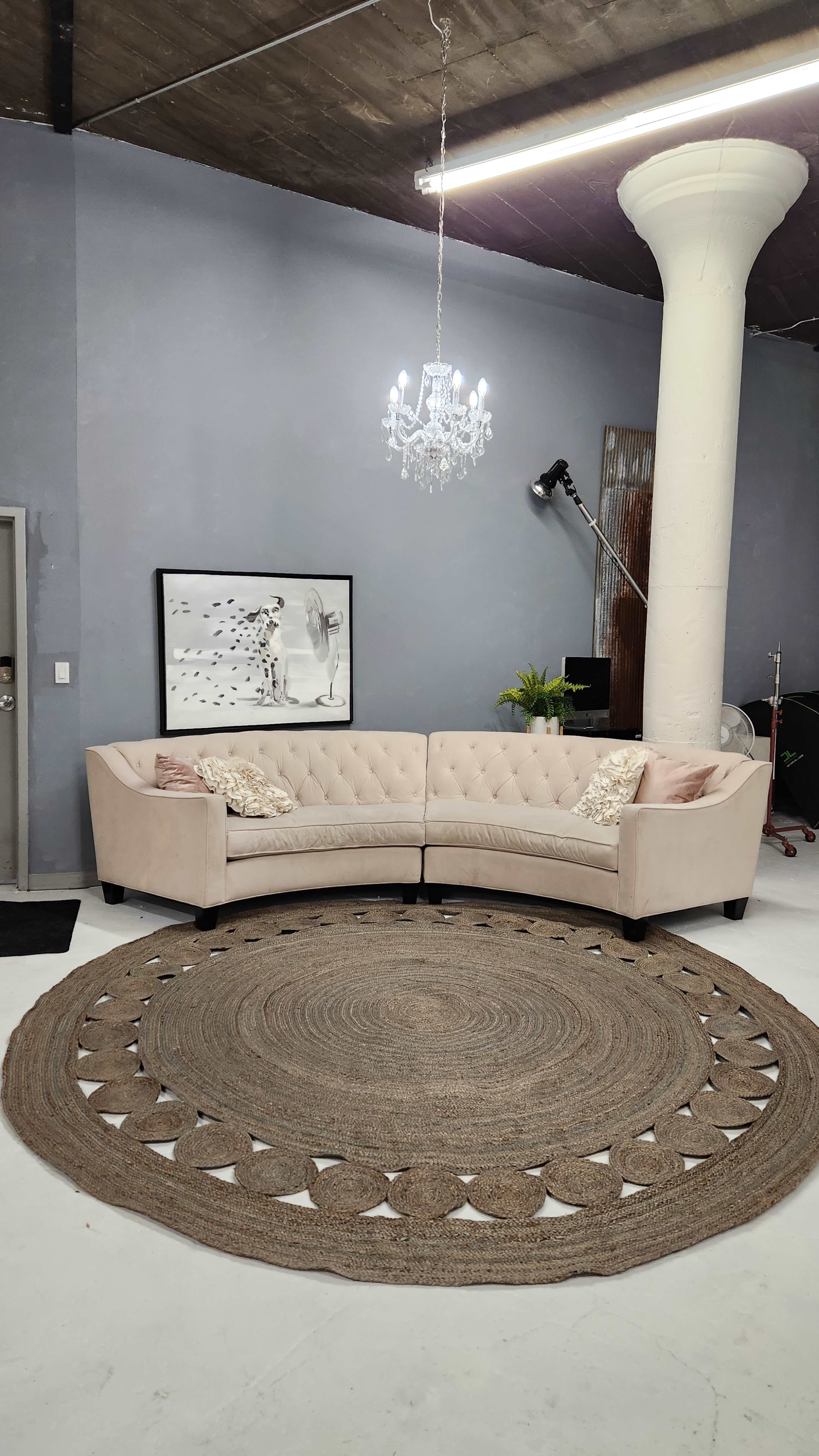 A modern interior with a light-colored, tufted sectional sofa placed on a round woven rug beneath a chandelier in a spacious room.