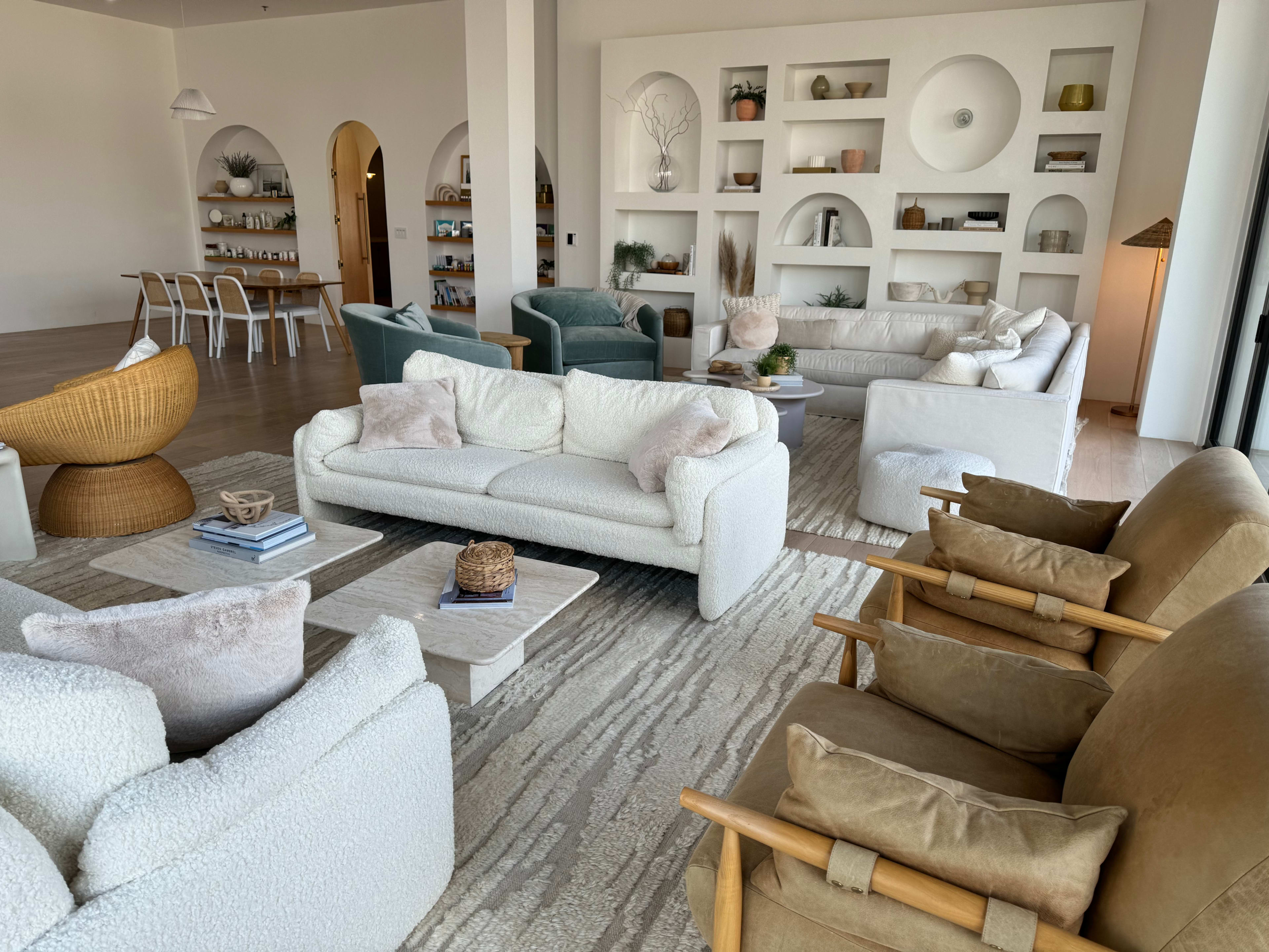 A spacious living room with multiple seating arrangements, including plush sofas and armchairs, and shelves displaying decorative items.