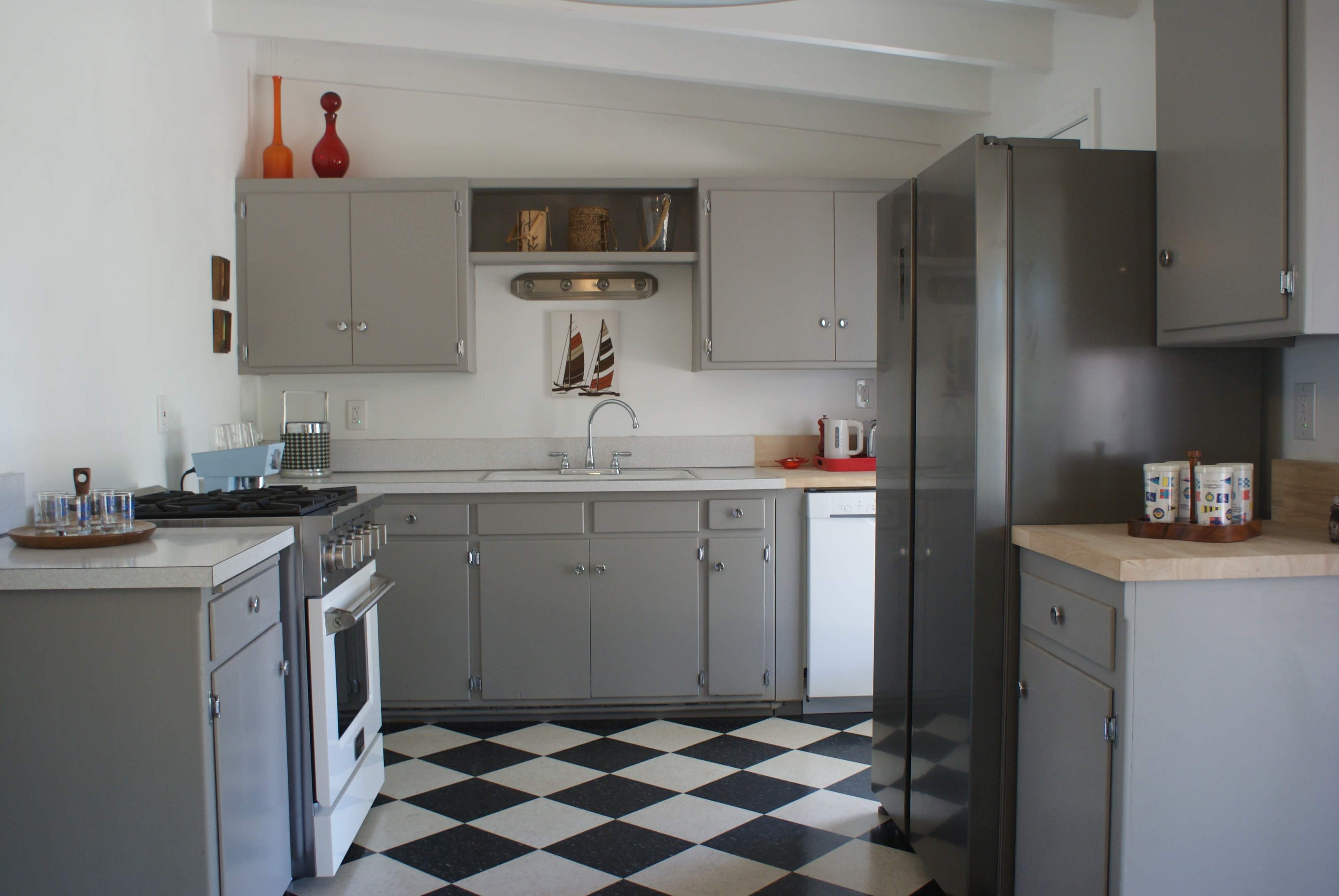 A modern kitchen with gray cabinetry, a stainless steel refrigerator, a black and white checkered floor, and simple decorative elements on the shelves.