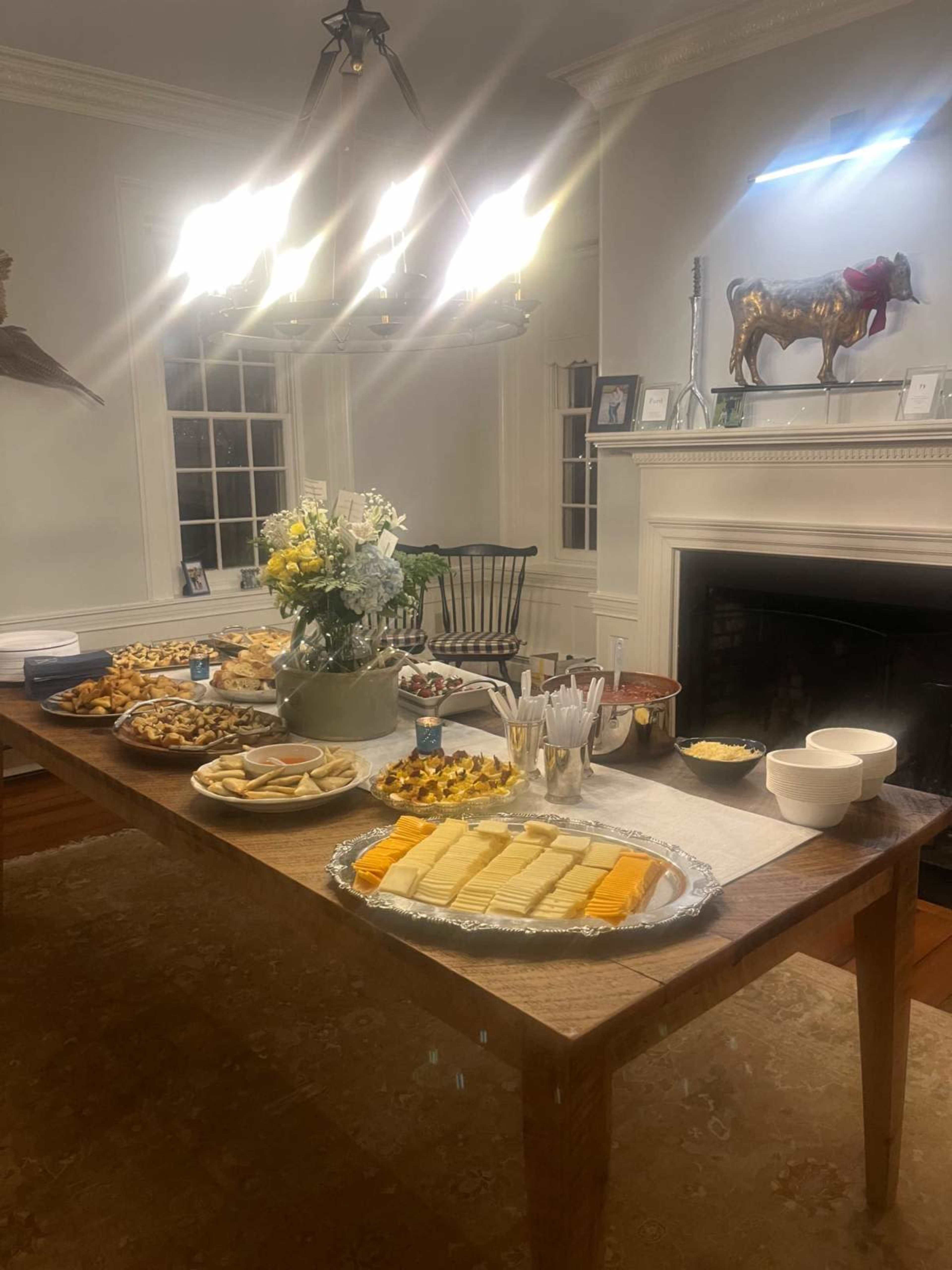 A dining table is set with an array of food, including cheese platters, fruits, and snacks, in a well-lit room with decorative items on the walls.