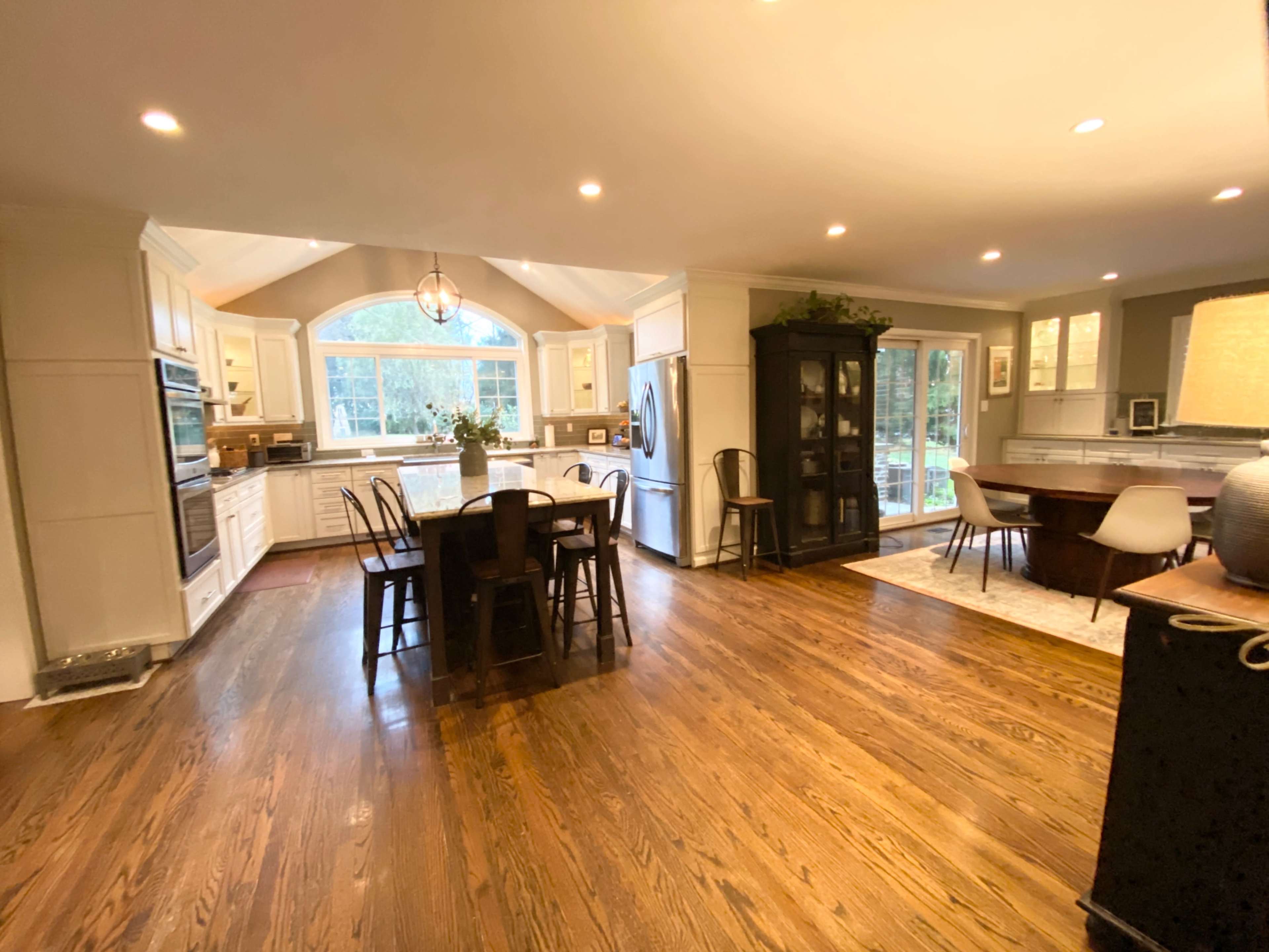 A spacious kitchen with white cabinetry, a large island with seating, and a dining area that features a glass door leading to a patio.