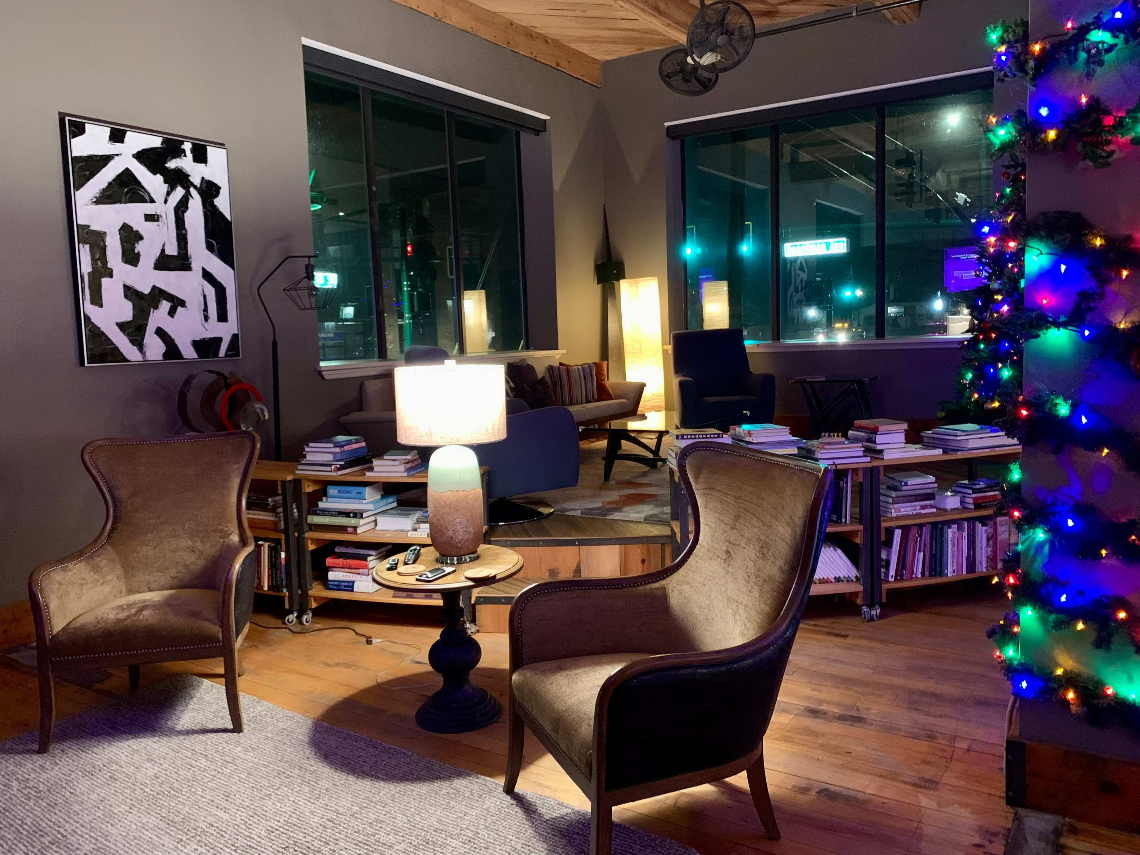 A cozy living space with two armchairs, a coffee table, bookshelves filled with books, and a decorated Christmas tree glowing with lights.