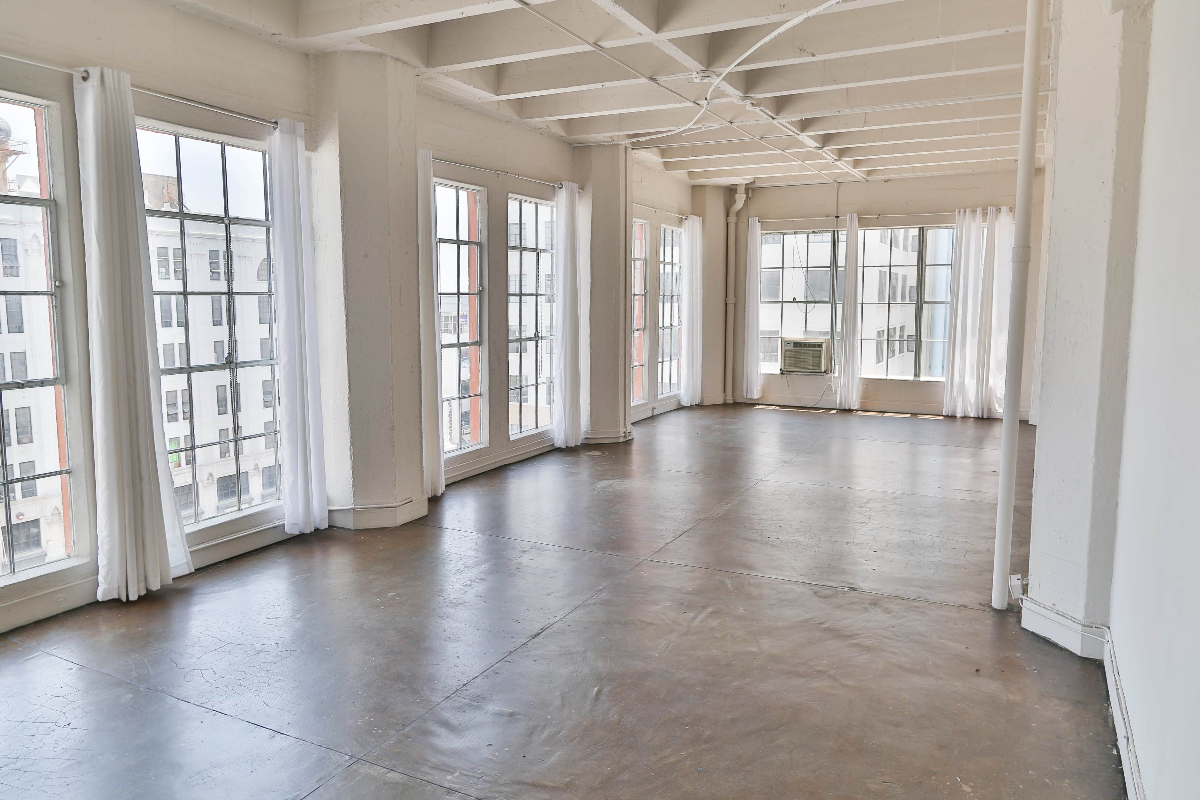 The spacious room features large windows with sheer curtains and a polished concrete floor.