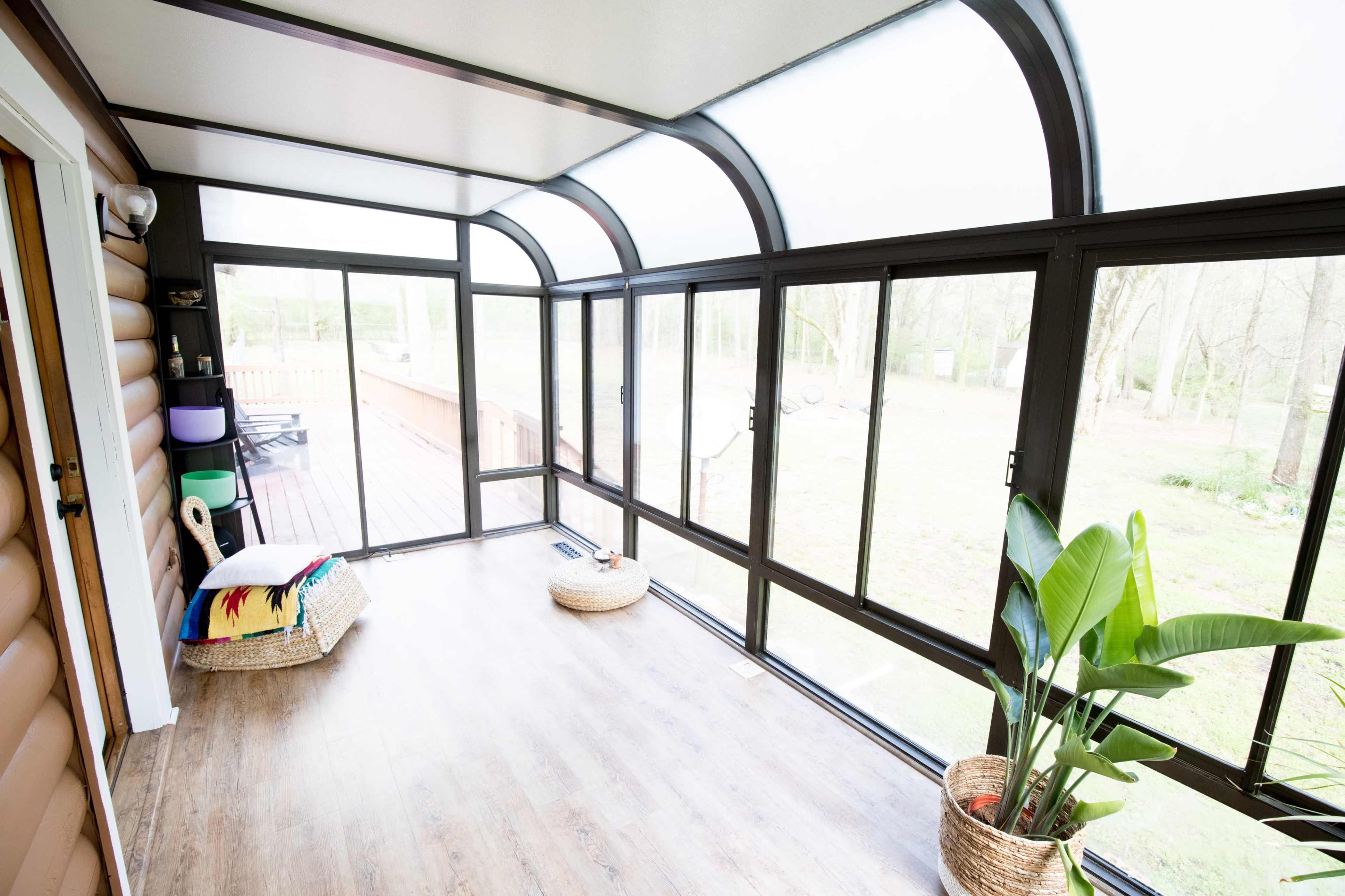 A sunroom with large windows, a wooden floor, and a view of a grassy backyard, featuring a seating area and potted plants.