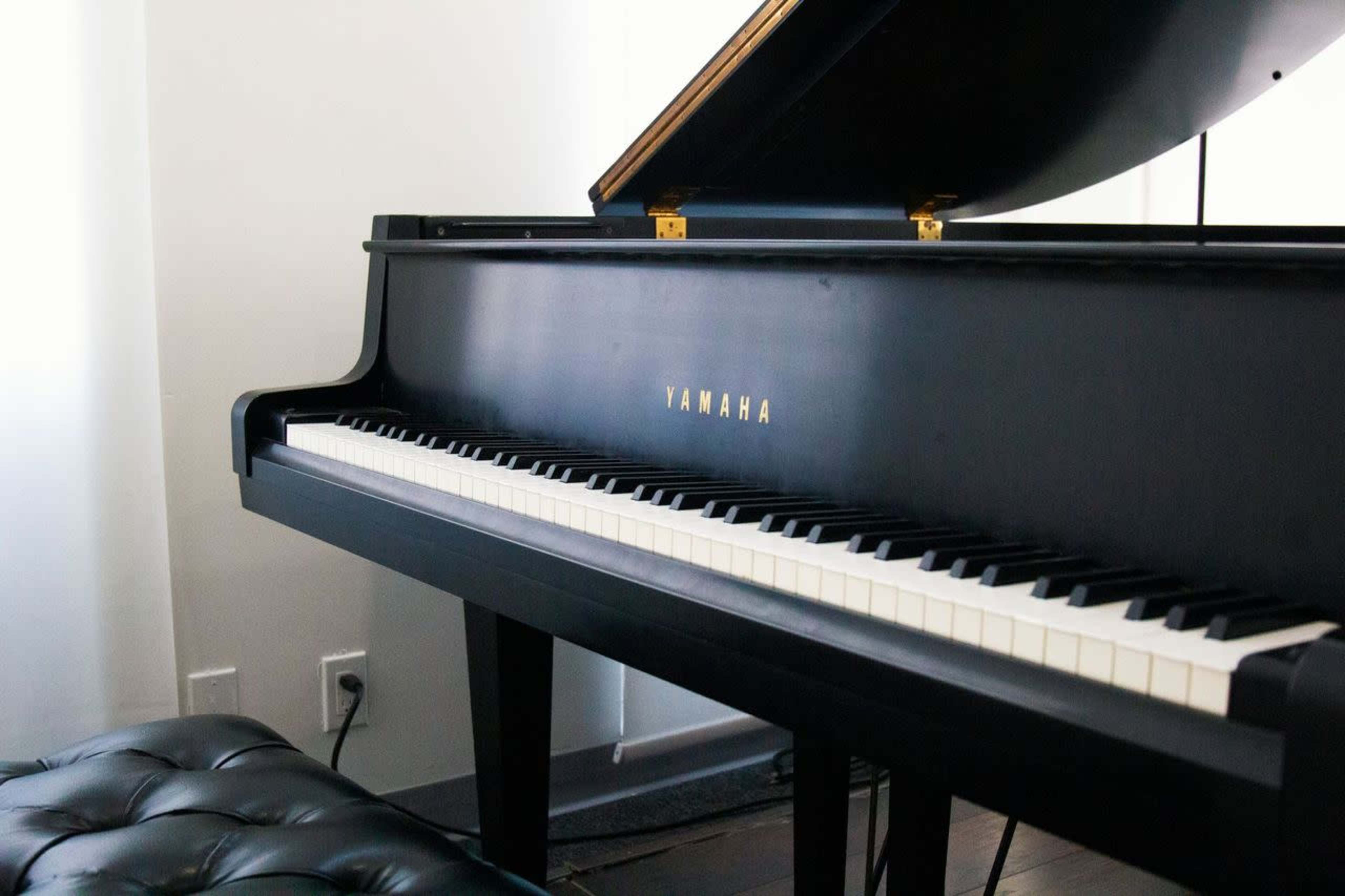 A black Yamaha grand piano sits beside a tufted leather bench in a bright room.