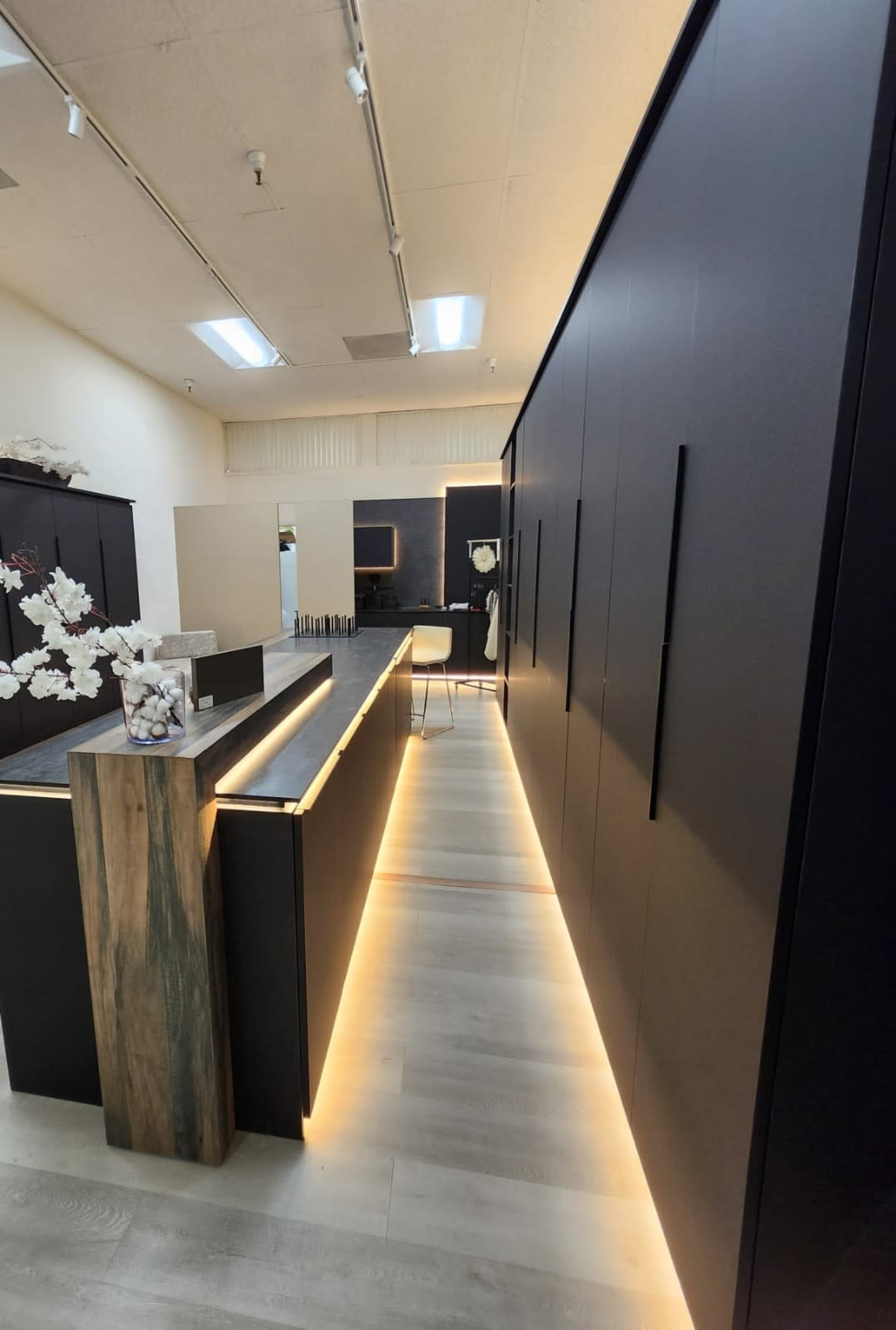 The image shows a modern interior space featuring sleek black cabinetry with a wooden accent along a well-lit corridor.