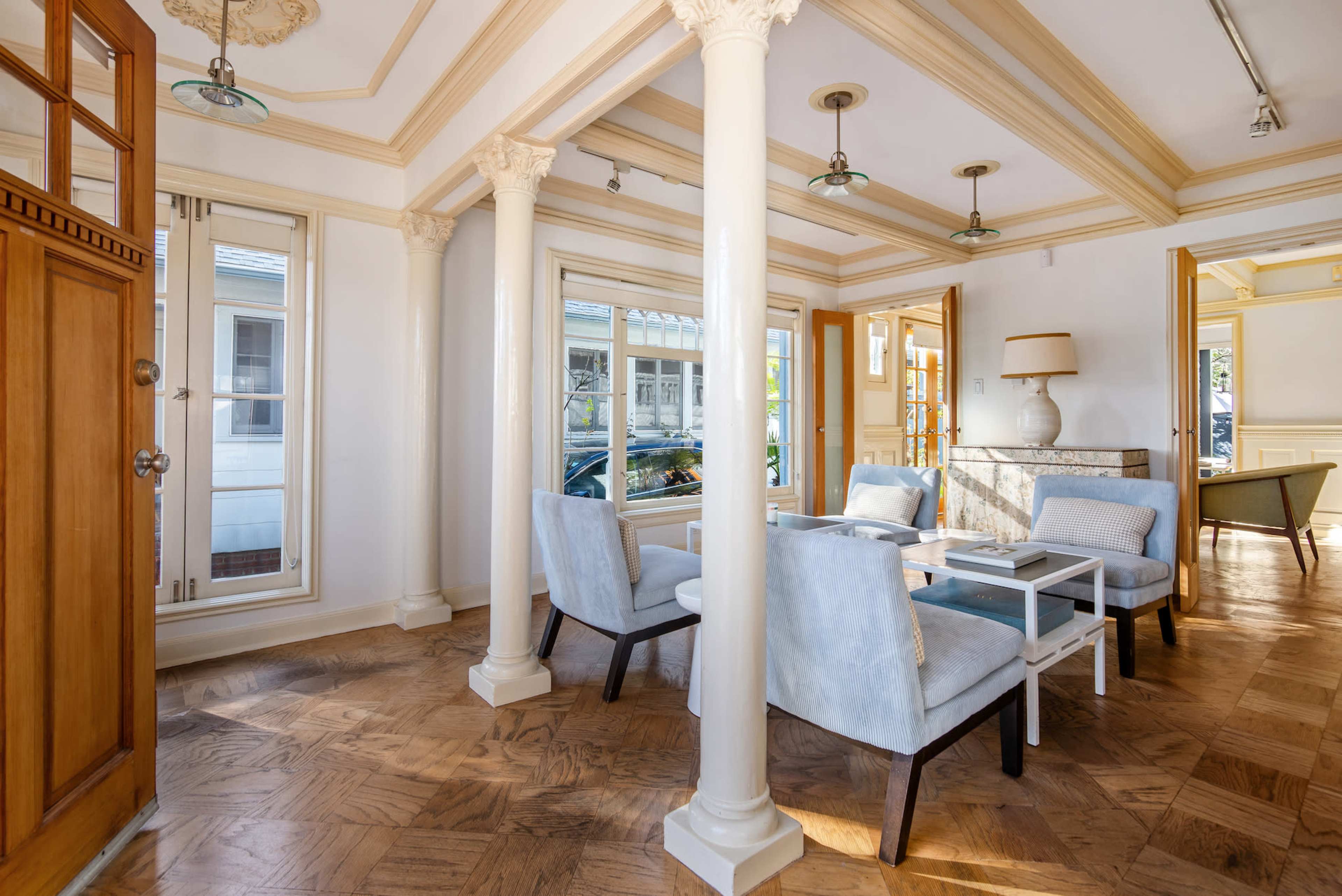 A bright, elegantly designed interior room with four upholstered chairs arranged around a white table, framed by large windows and decorative columns.