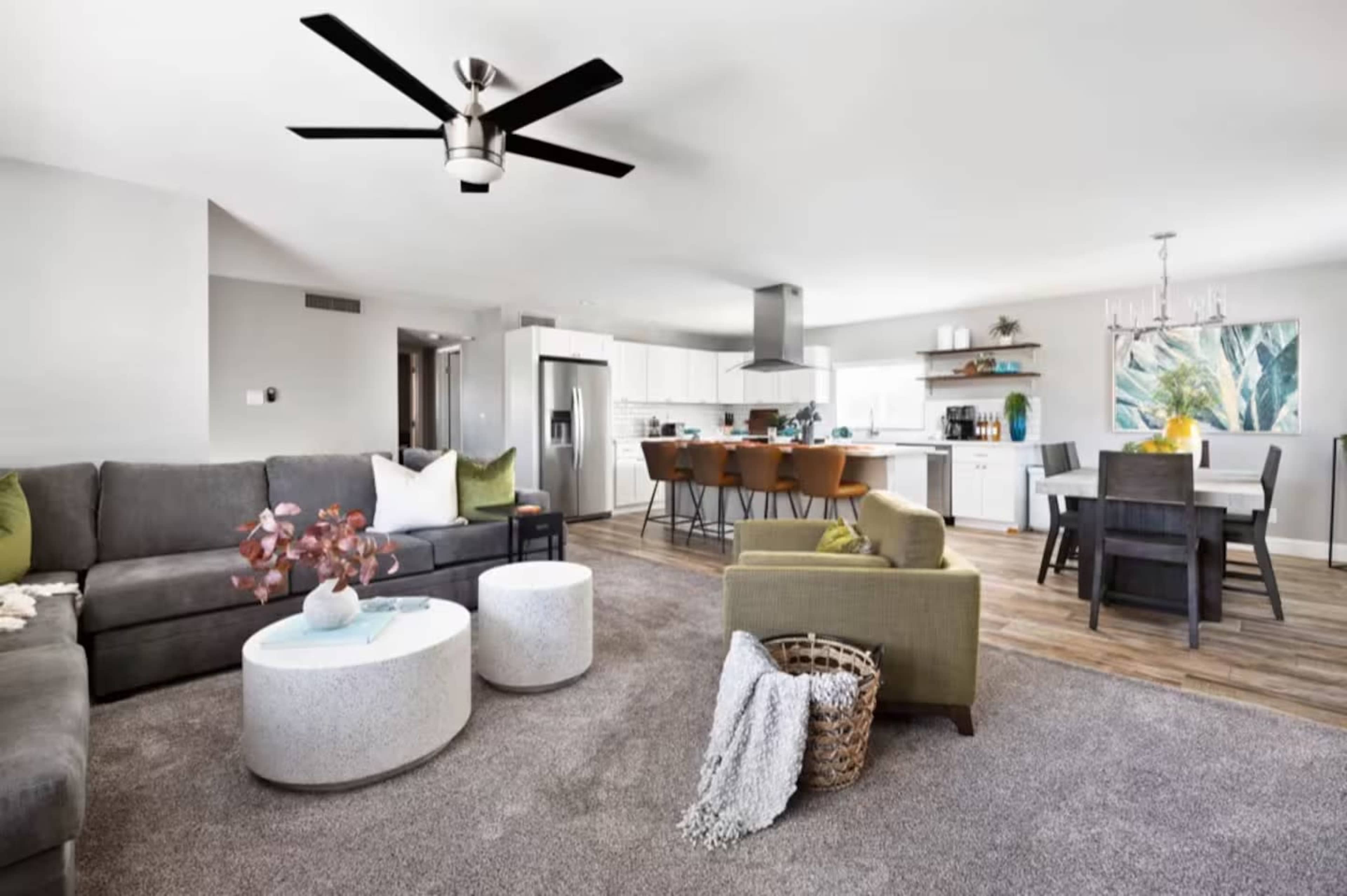 The living room features a gray sectional sofa, two round coffee tables, and an open kitchen with a dining area, showcasing modern furnishings and decor.
