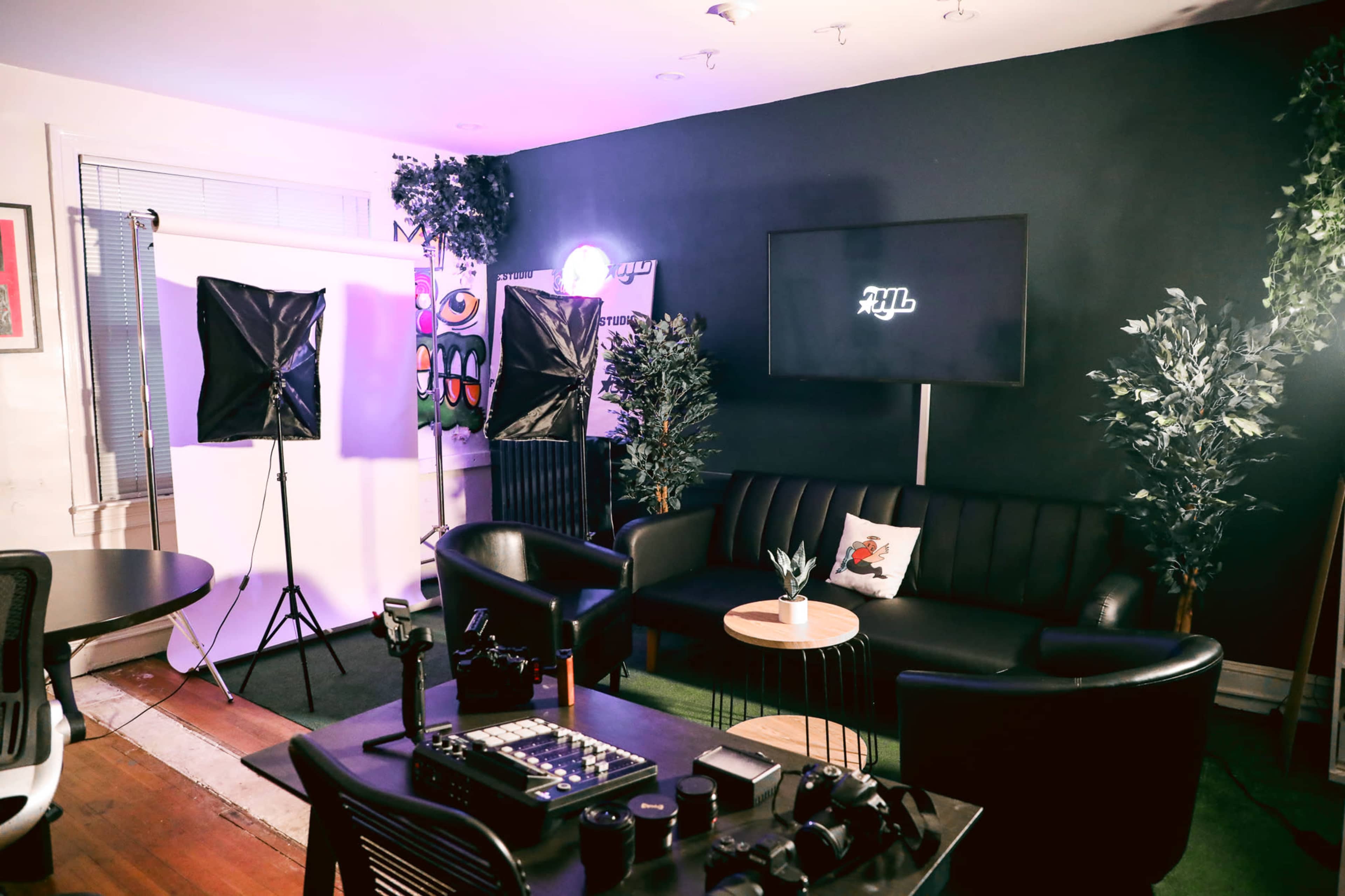 A modern studio setup features a black sofa, two softbox lights, a television screen, and various camera equipment arranged on a table.