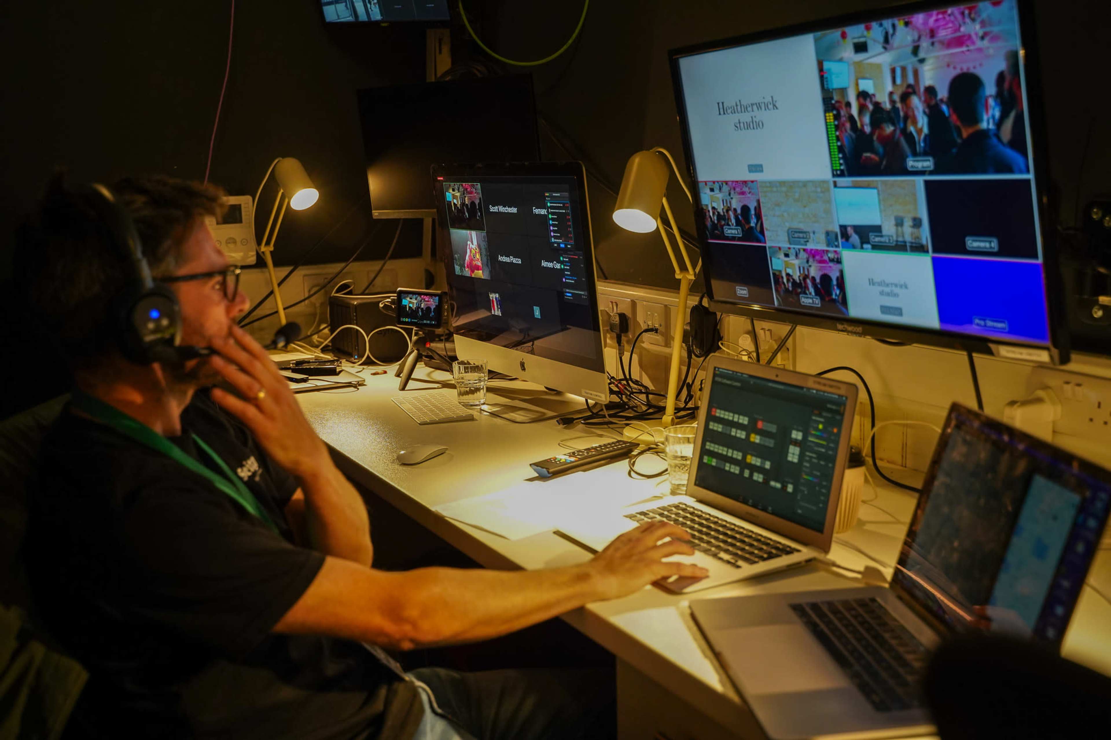 A person wearing headphones operates multiple computer screens in a control room setting.
