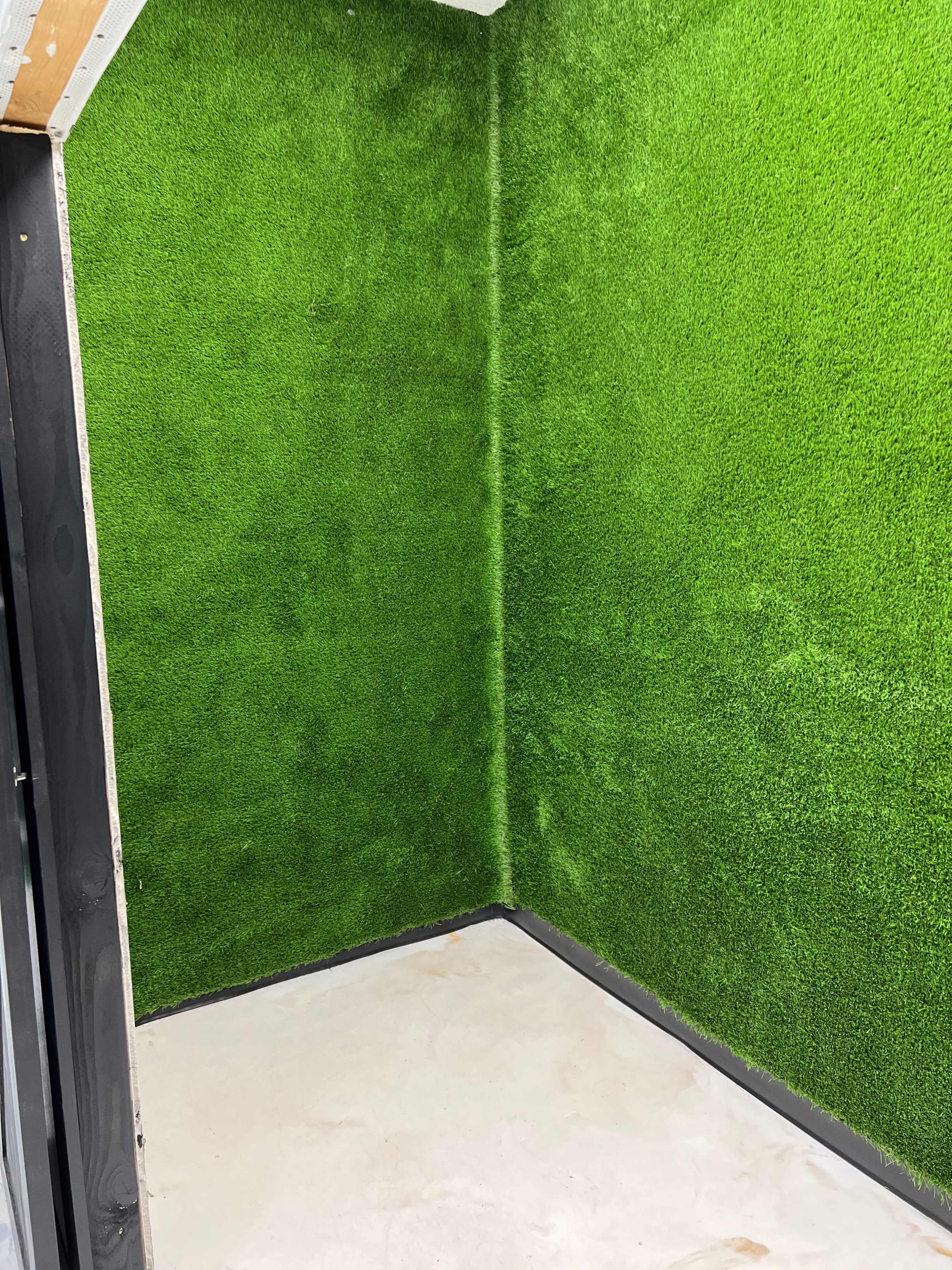 A corner of a room with bright green artificial grass covering the walls and a bare concrete floor.