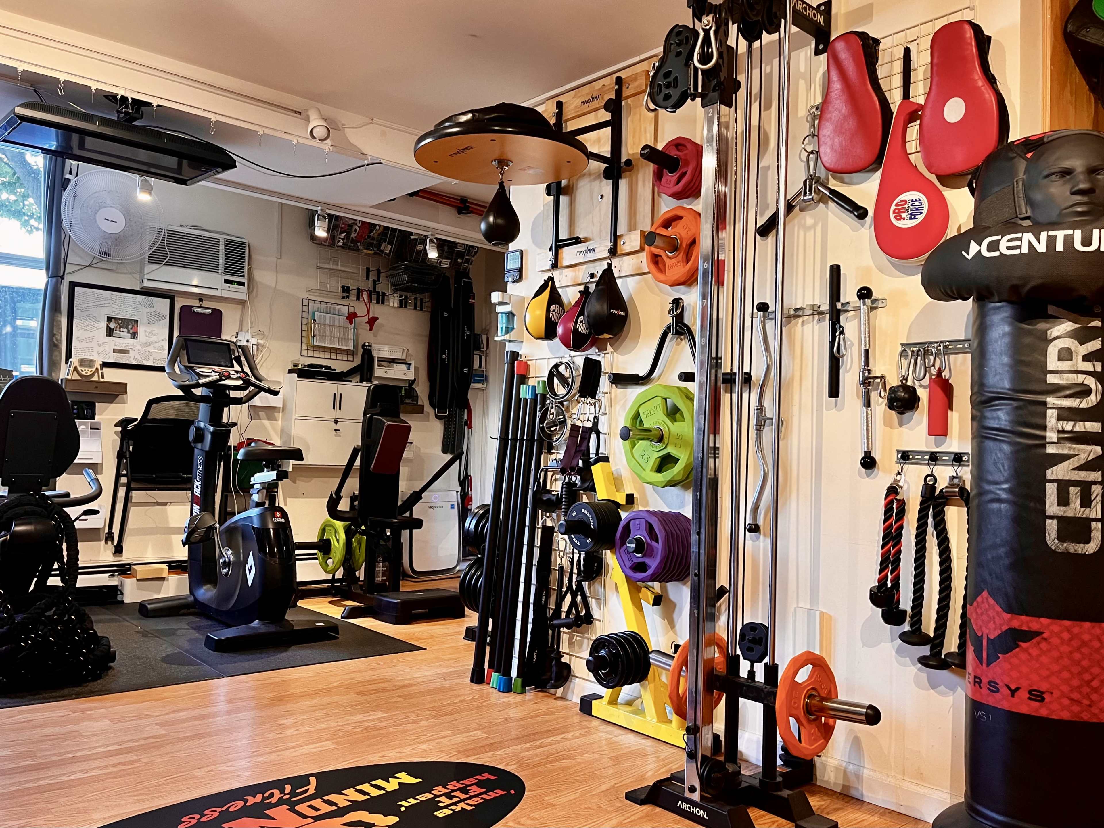 A home gym equipped with various exercise machines, weights, and hanging workout accessories organized on walls.
