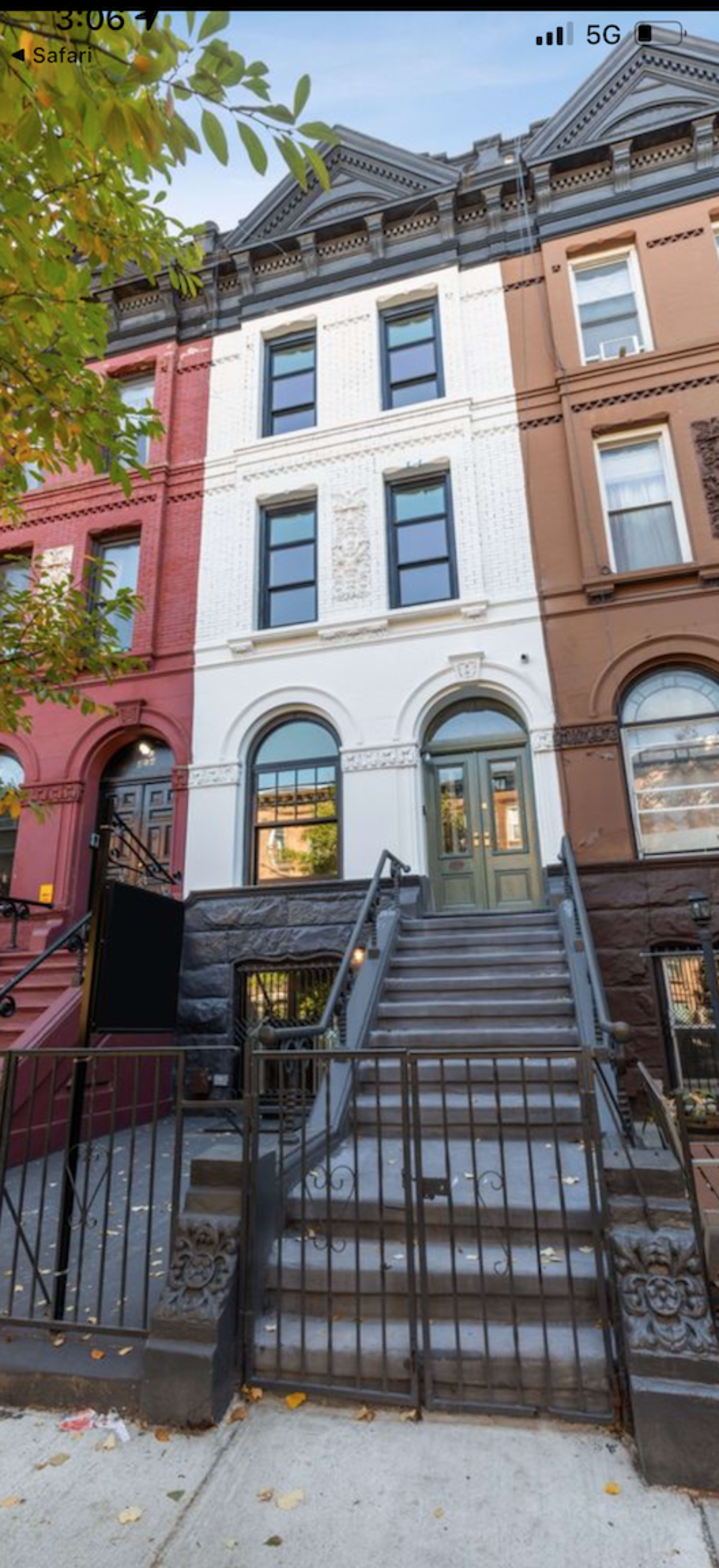 The image shows a row of brownstone townhouses, with a focus on one building featuring three large windows and a central entrance, flanked by white and red brick exteriors.