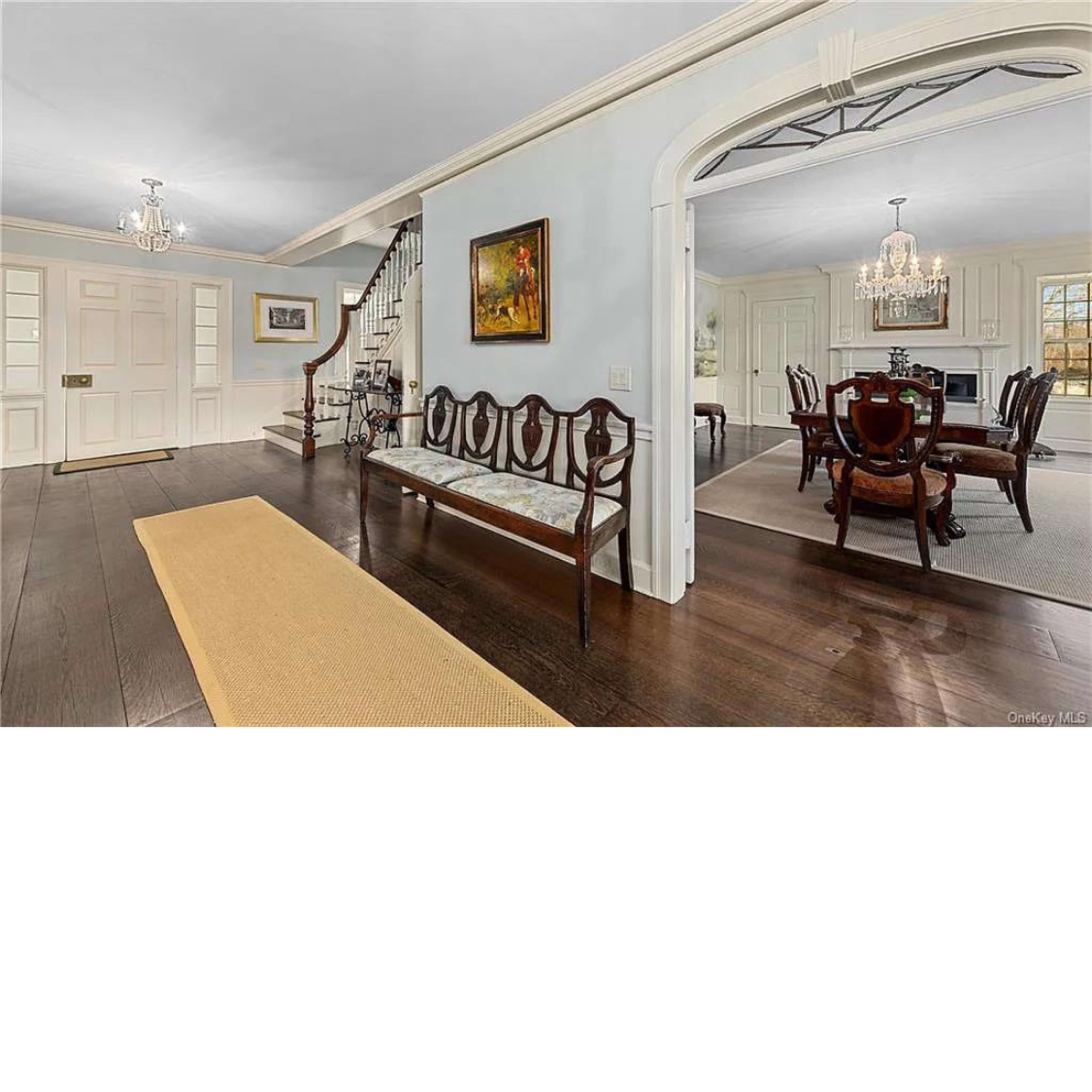 An inviting foyer with a wooden bench, a staircase leading to an upper floor, and visible dining areas in the background.