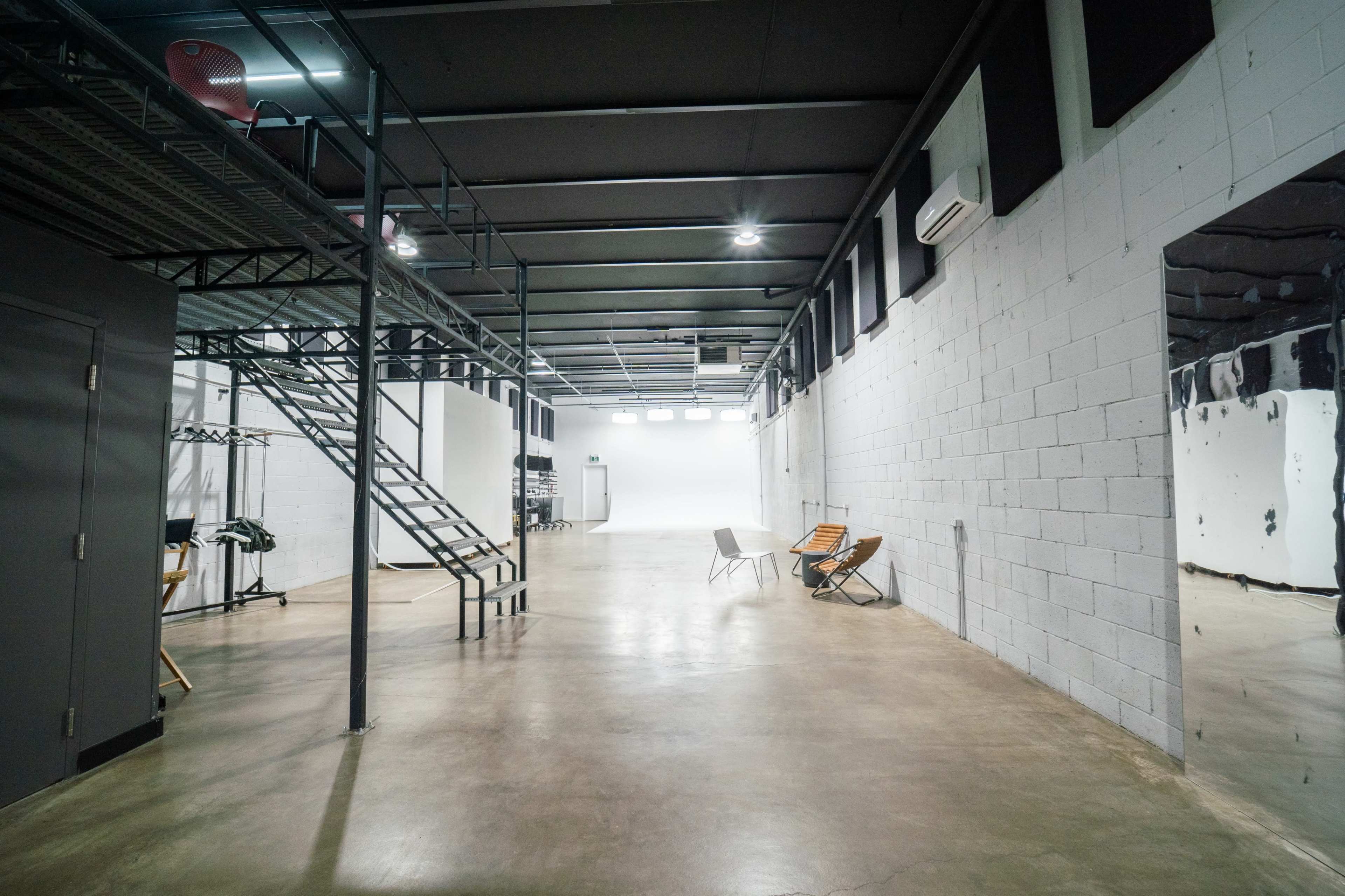 An industrial-style studio space with a staircase, gray walls, and chairs arranged along one side.