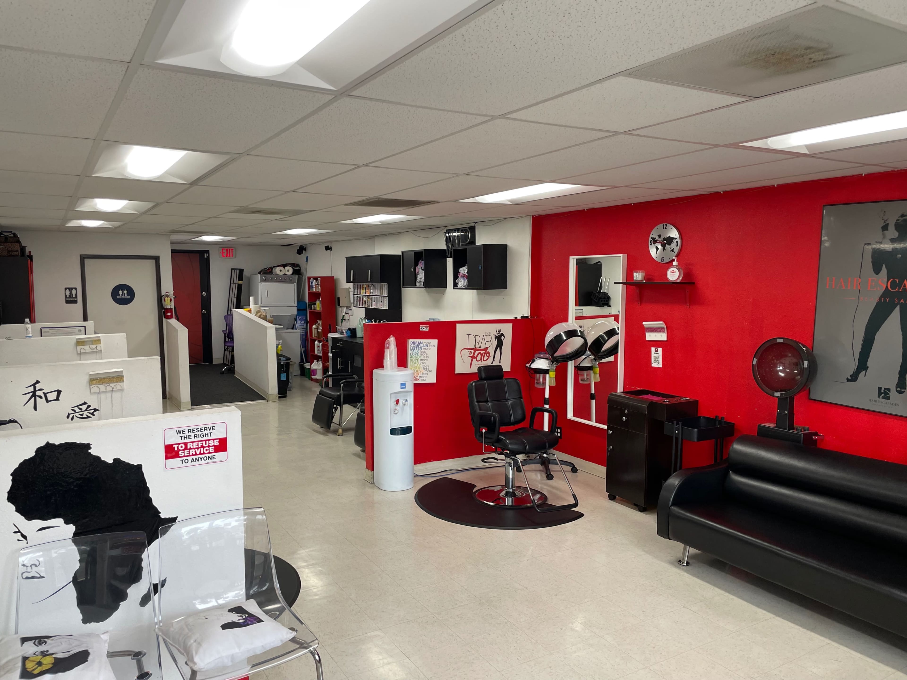 A brightly lit salon with black and red decor, featuring styling chairs, a reception area, and various hair care products on display.