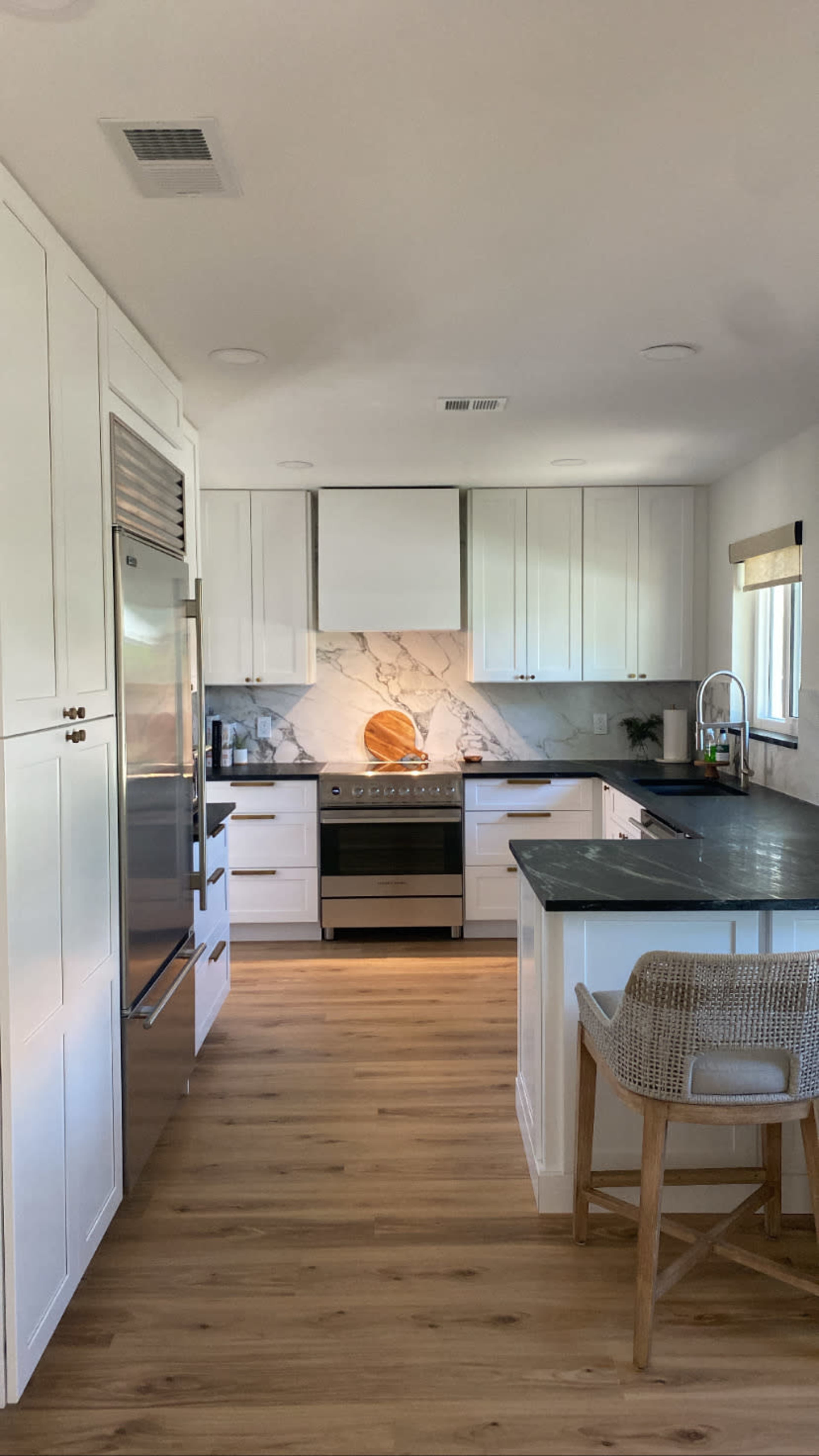A modern kitchen features white cabinetry, a marble backsplash with a circular wooden accent, stainless steel appliances, and wooden flooring.