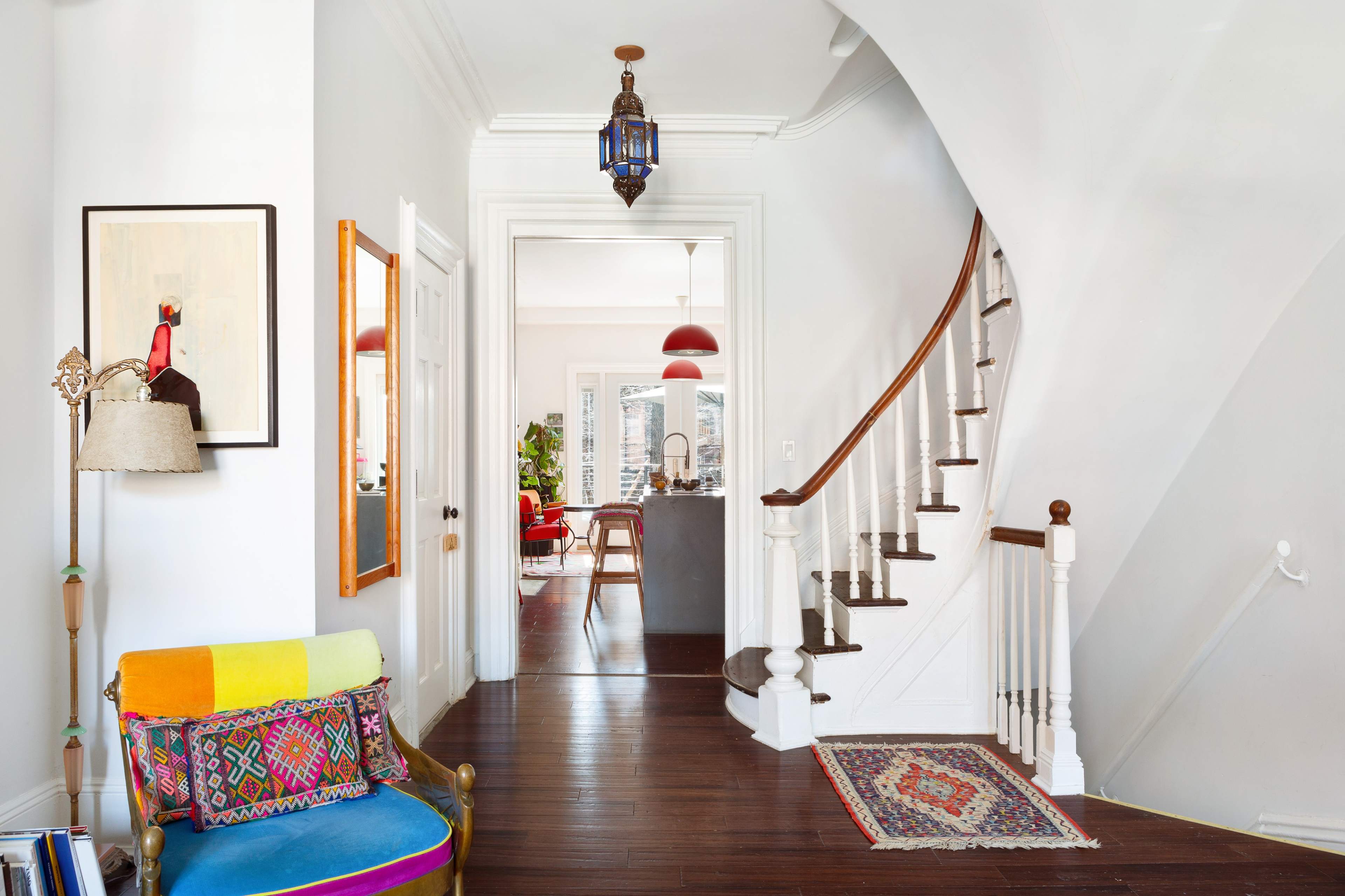 A bright entryway with a staircase, a colorful armchair, and an open view into a modern living space beyond.