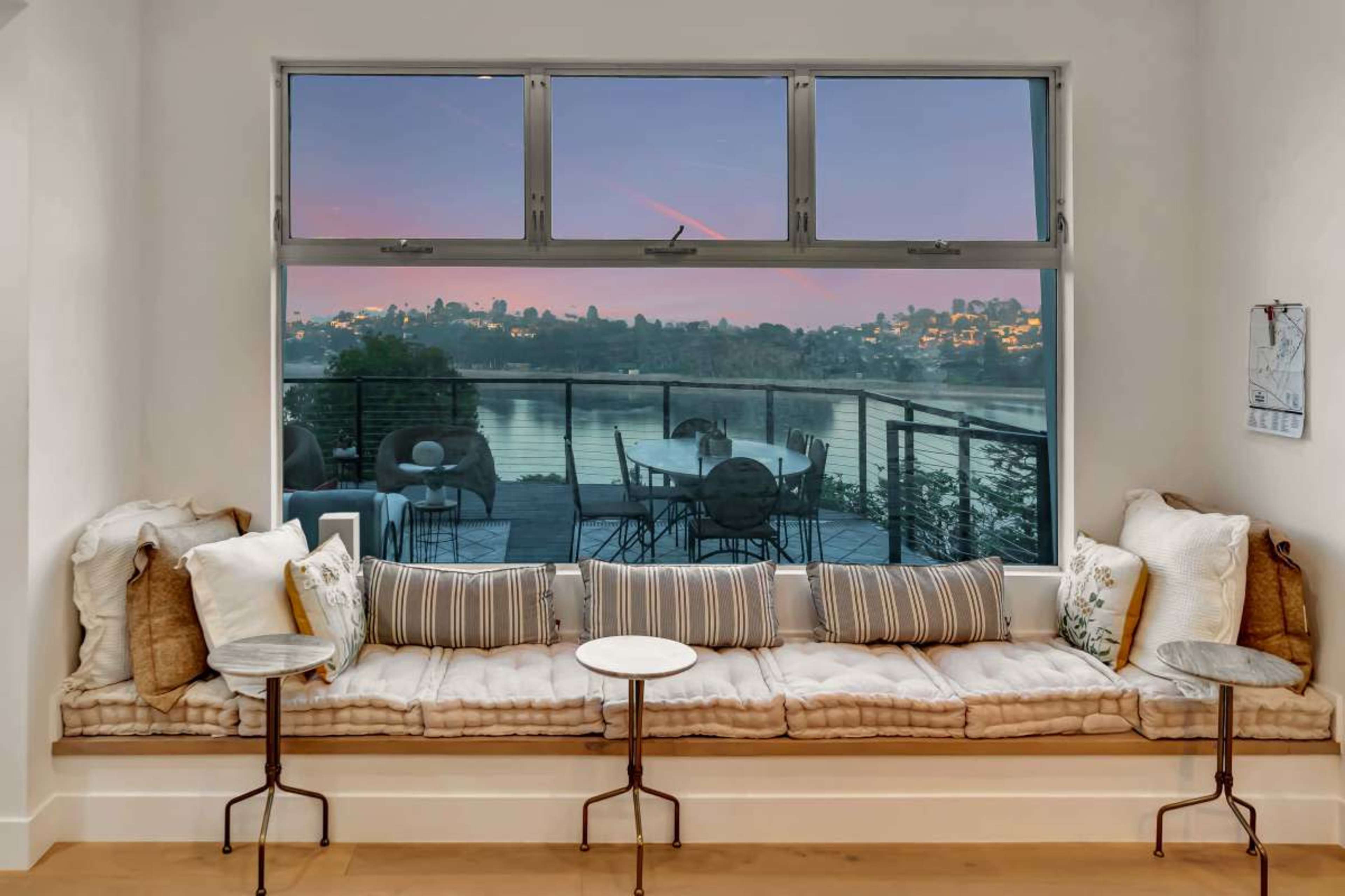 A cozy window seat with soft cushions overlooks a waterfront view at sunset.