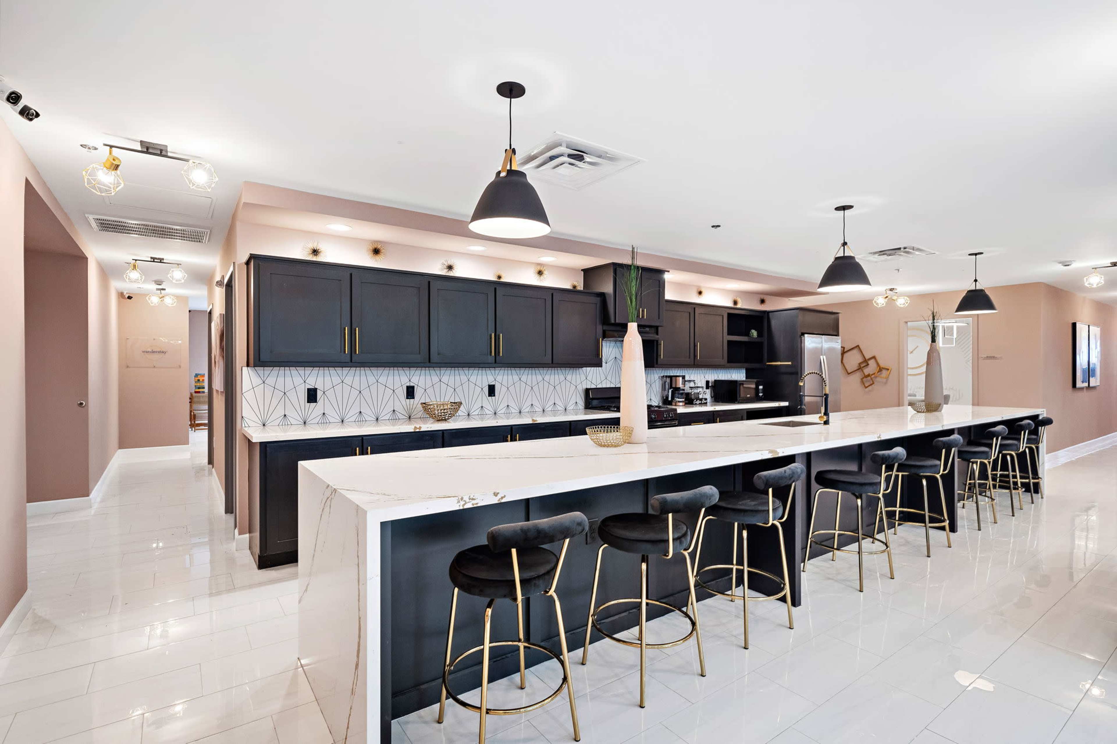 The image shows a modern kitchen with a large marble countertop and black cabinetry, featuring high stools along one side.