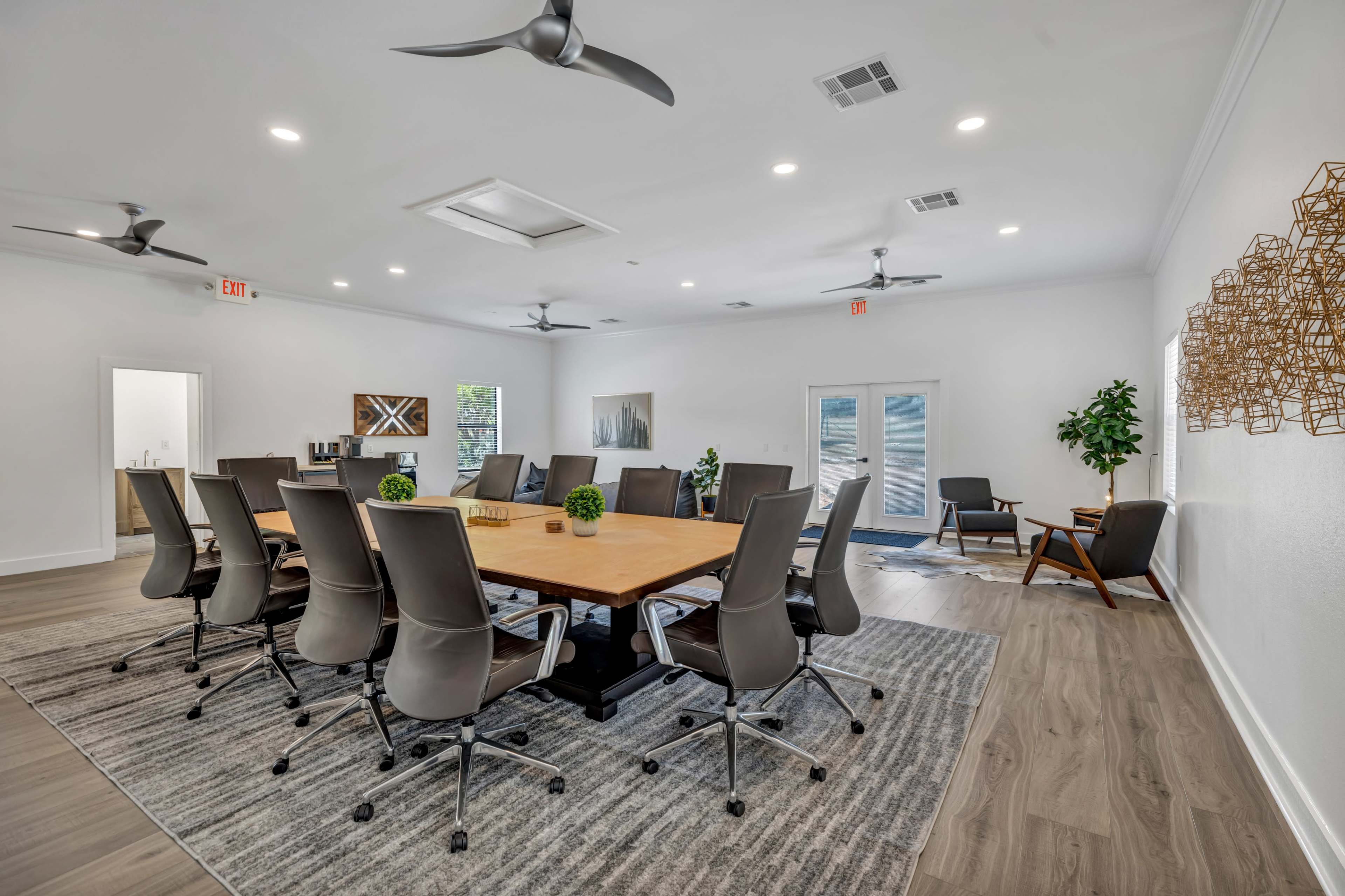 A large conference room features a central wooden table surrounded by ergonomic chairs, with a clean, modern design and large windows.