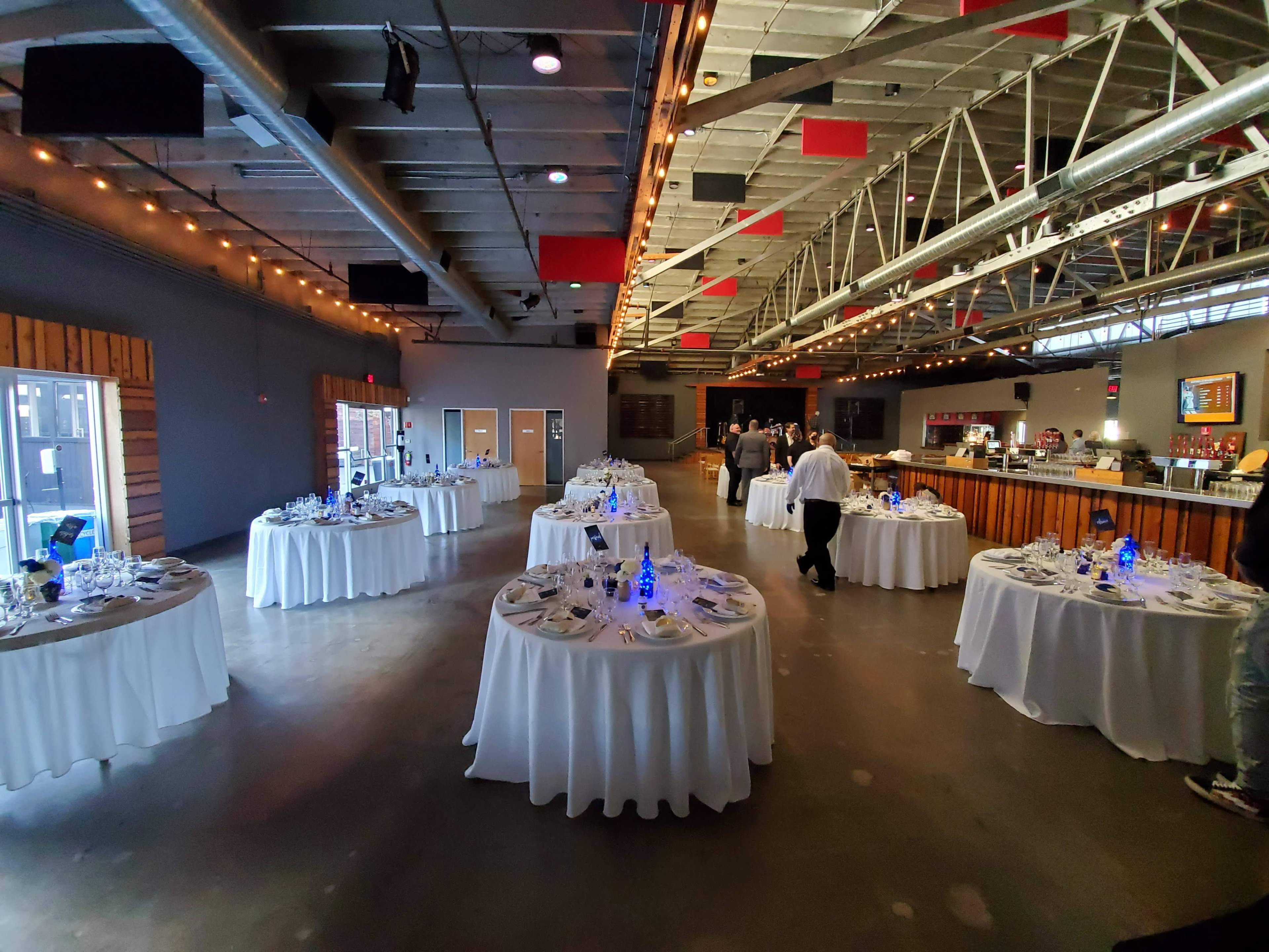 A spacious dining area with several round tables set for a formal meal, featuring white tablecloths and blue centerpieces.