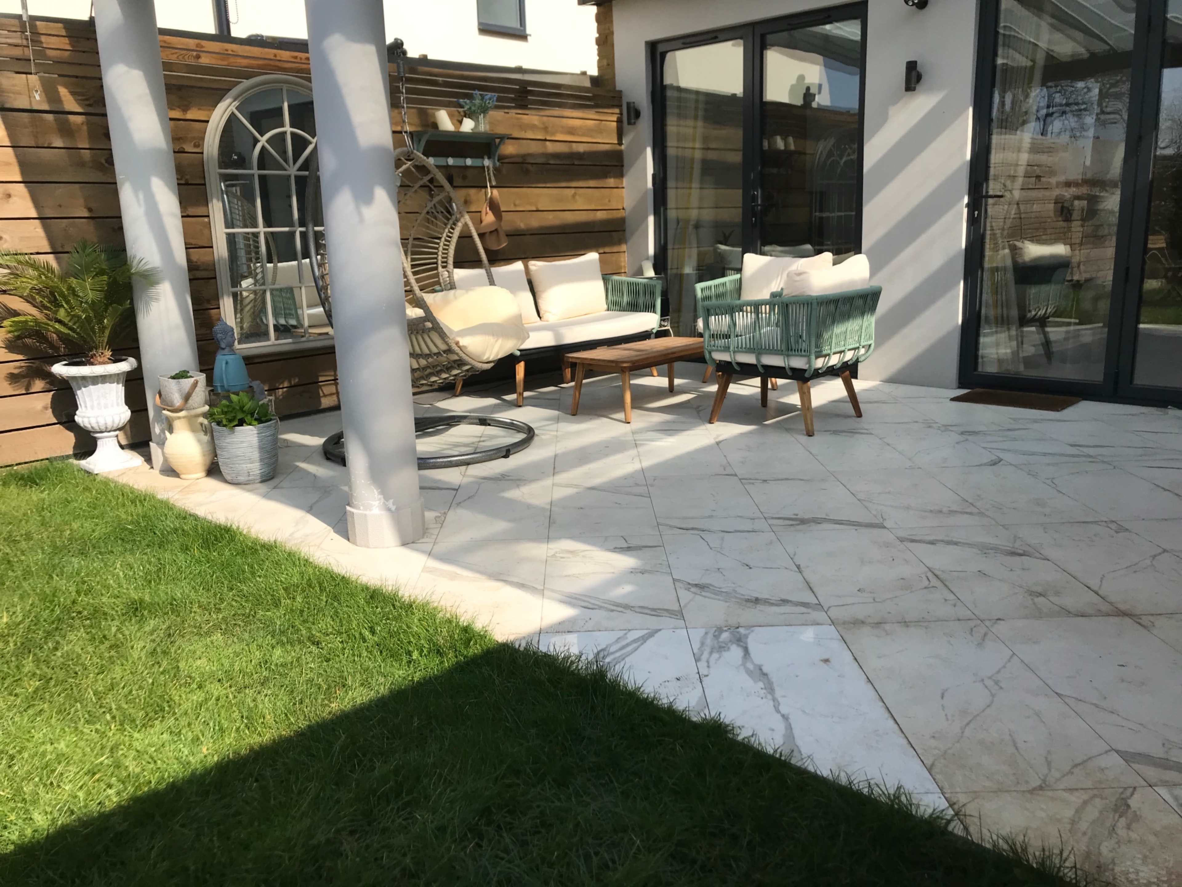 A modern outdoor patio features seating arrangements with a coffee table, surrounded by a well-maintained lawn and decorative plants.