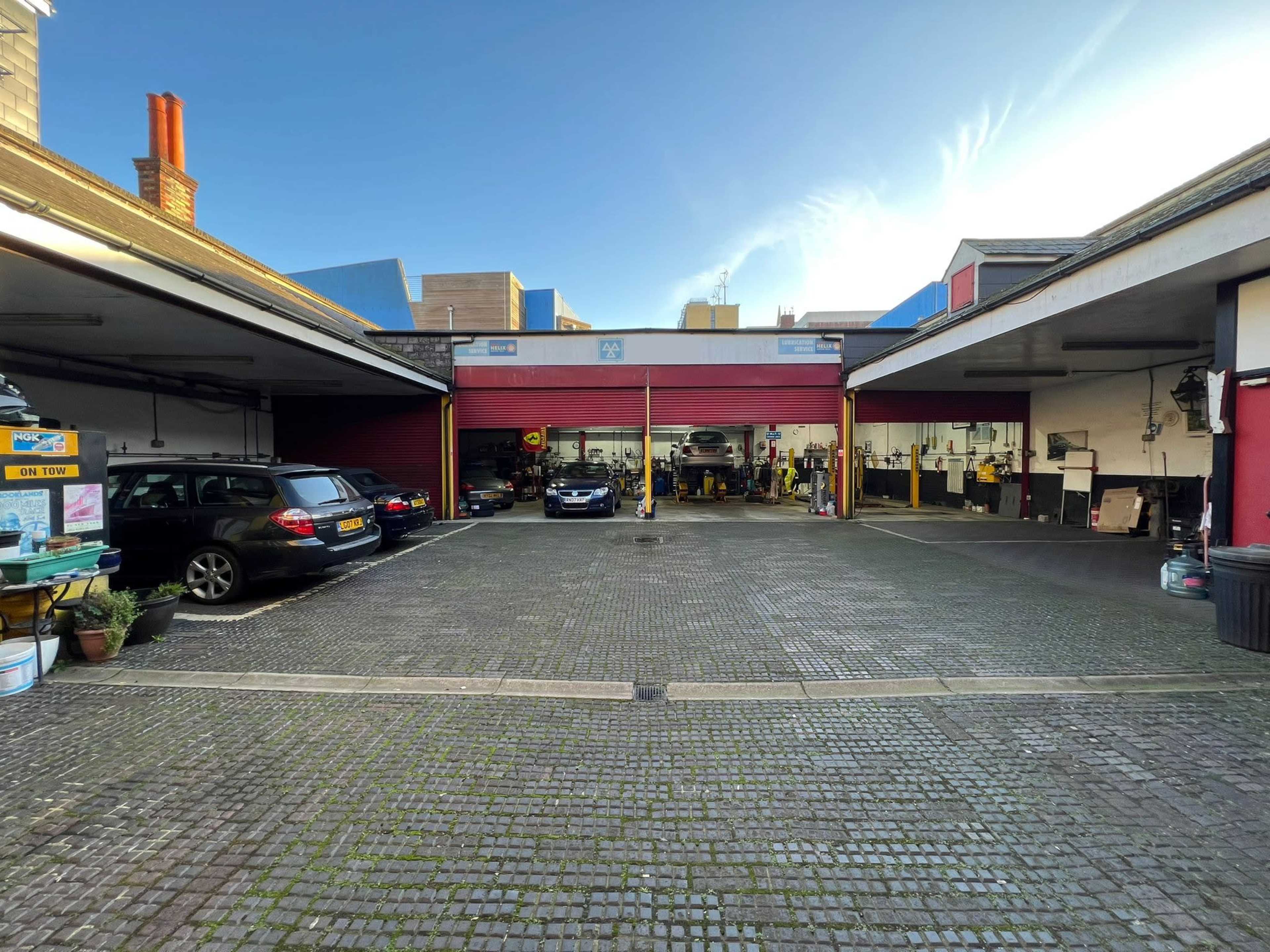 A garage area with parked cars and several workstations visible, set within a spacious, paved courtyard.