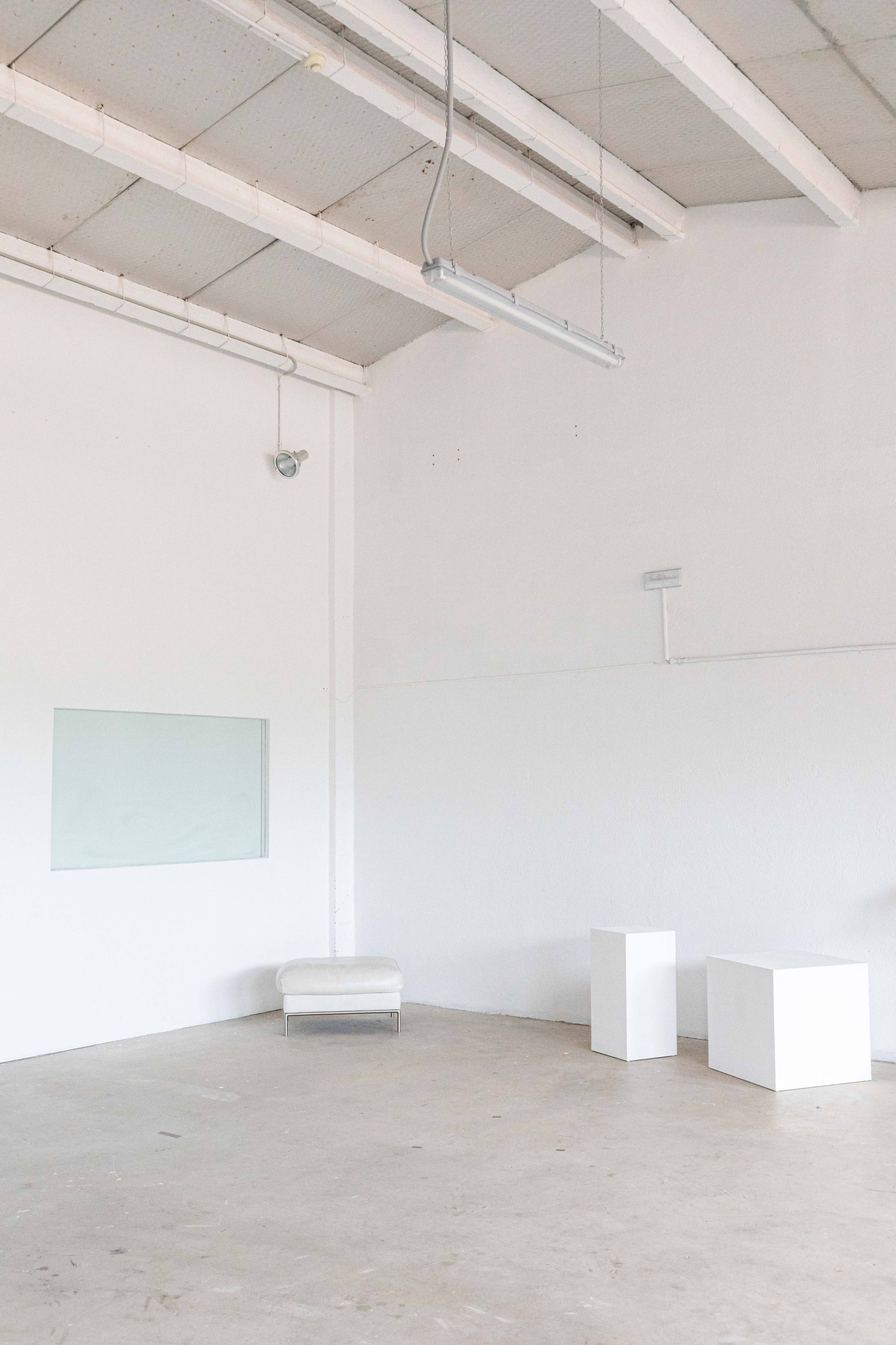 A minimalistic, empty room with white walls, a small window, and two white display pedestals.
