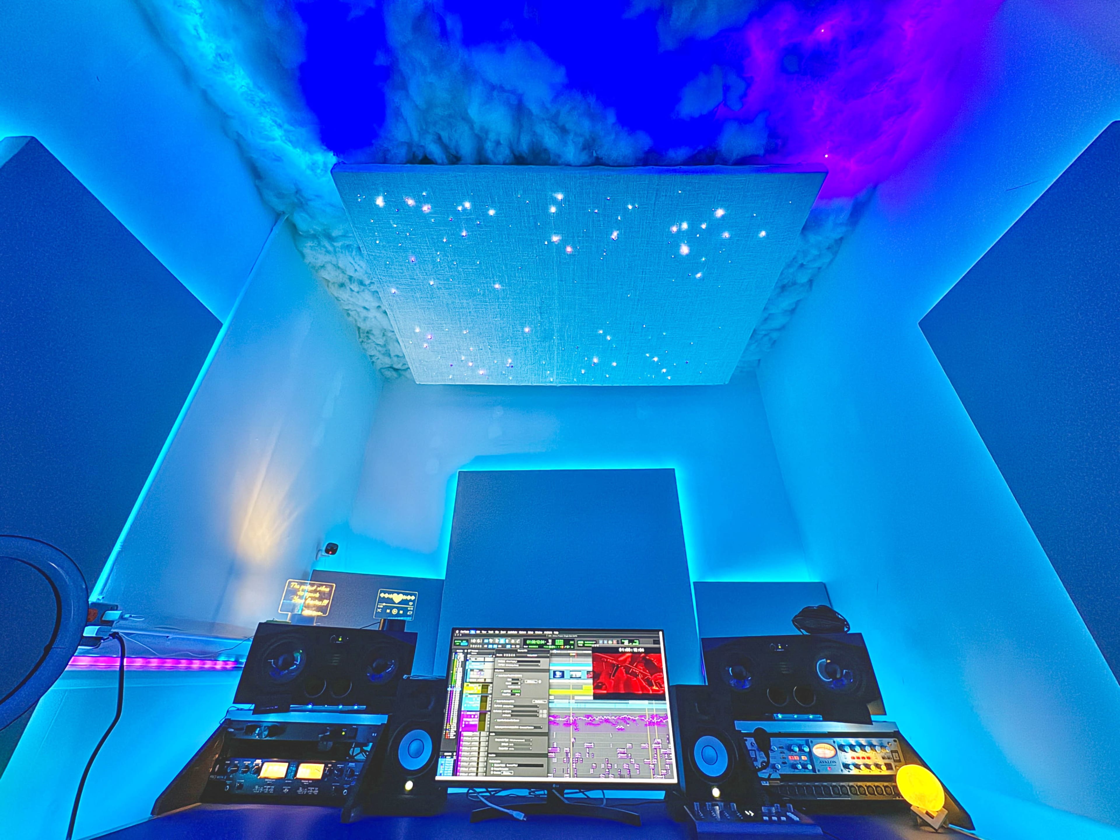 A modern music studio features two speakers and a computer monitor, with a starry sky ceiling and blue ambient lighting.