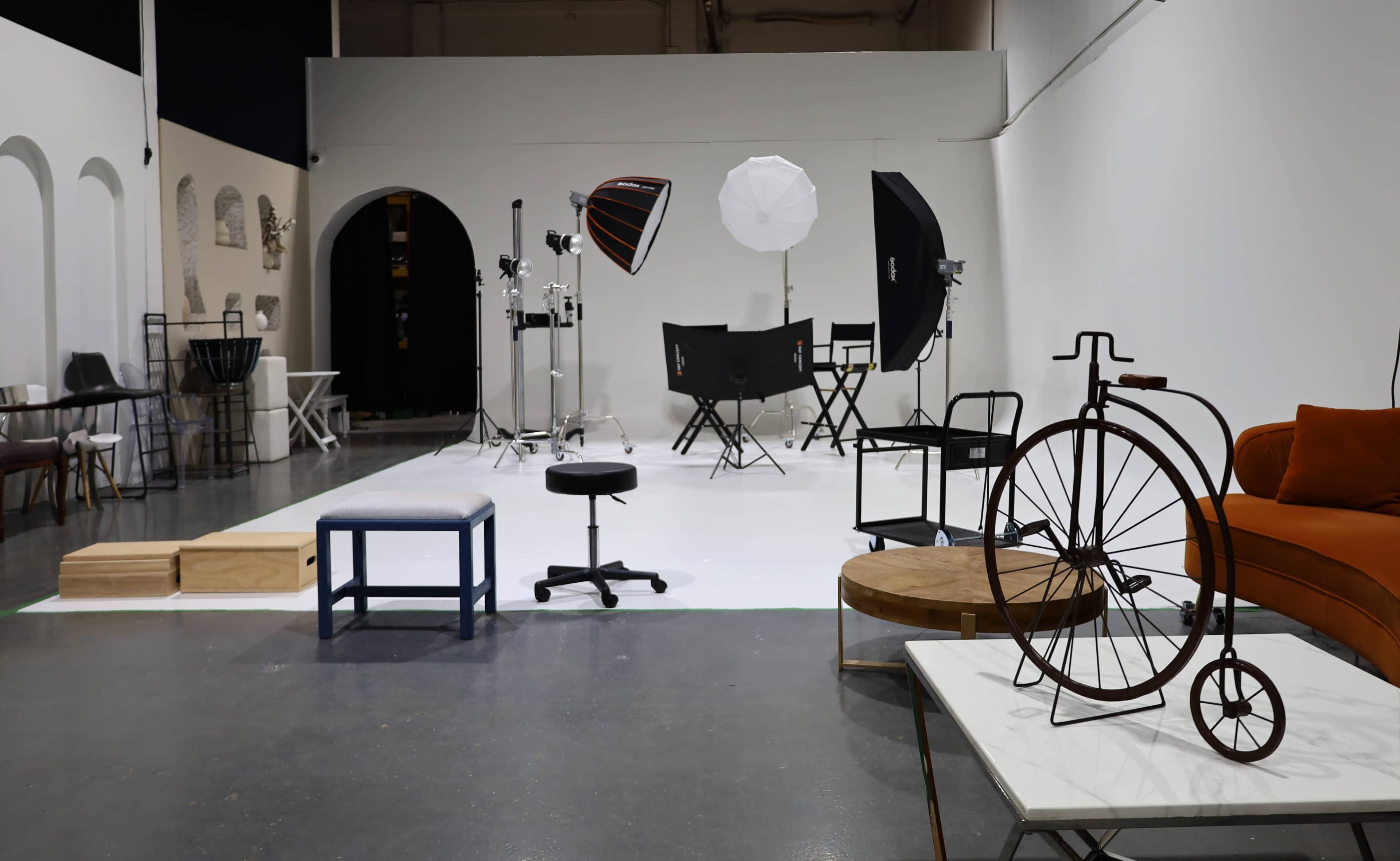 The image shows a spacious studio setup with various lighting equipment, backdrop, and furniture arranged for a photo shoot.