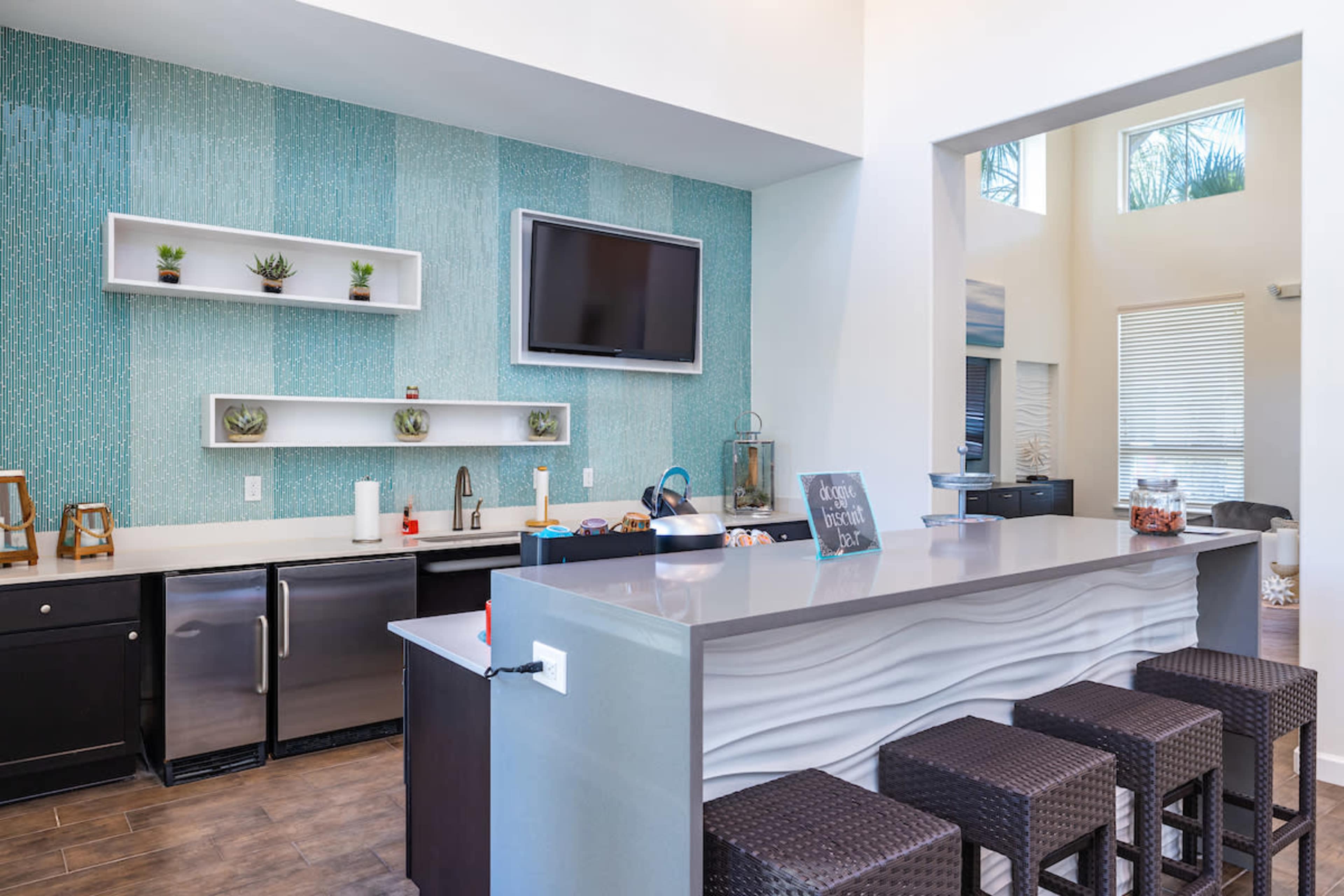 The image shows a modern kitchen with a light blue accent wall, stainless steel appliances, and a gray island with woven stools.