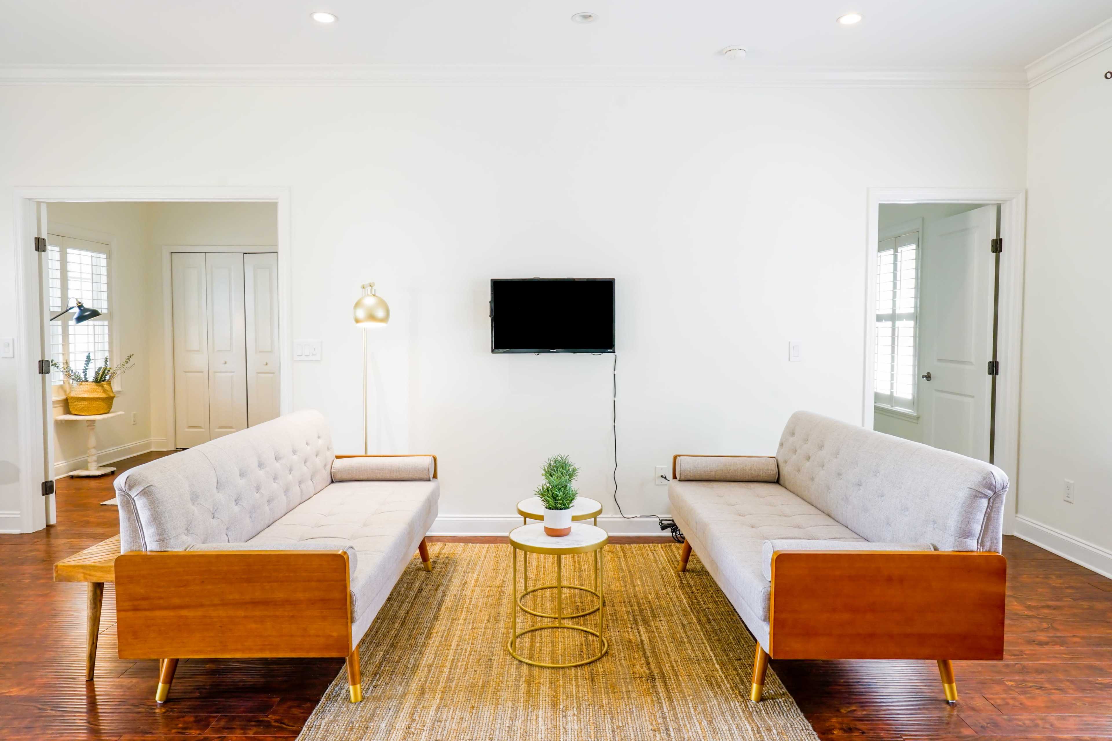 A modern living room with two gray sofas facing a small round table, a potted plant on the table, and a television mounted on the wall.