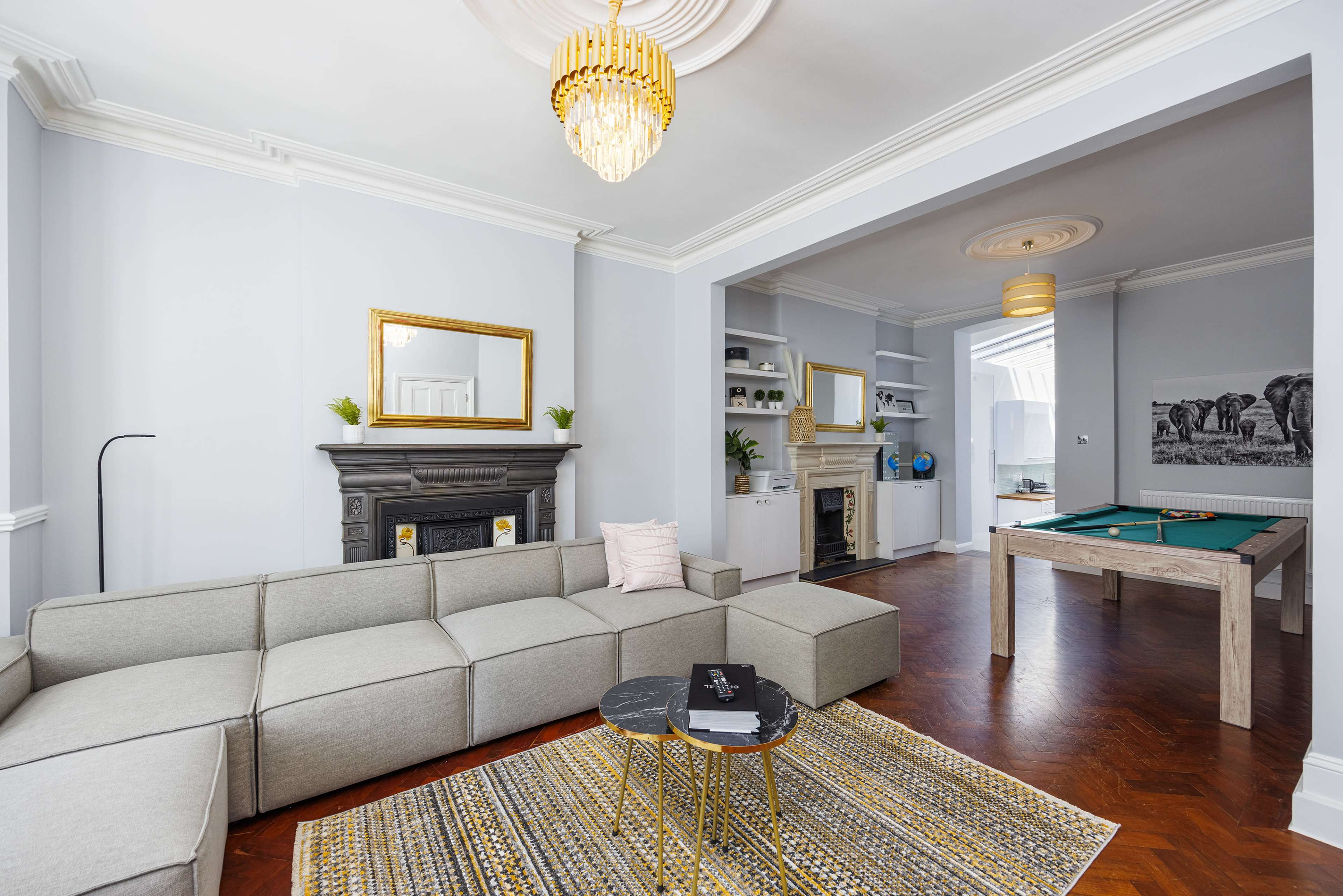 The image features a modern living room with a sectional sofa, a coffee table, and a view of an adjoining game area with a pool table.