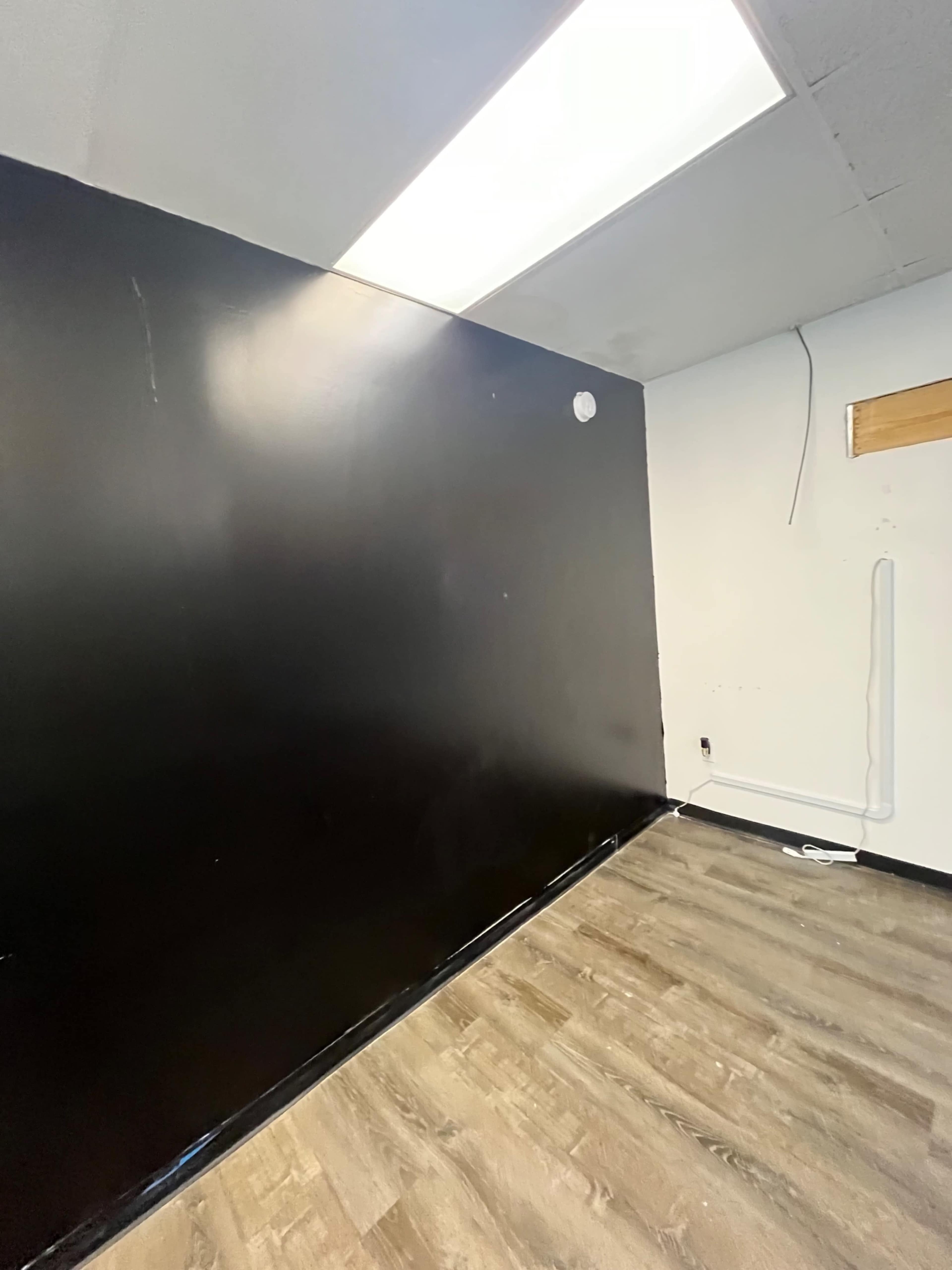 A room with a black wall, a light source from the ceiling, and wooden flooring.