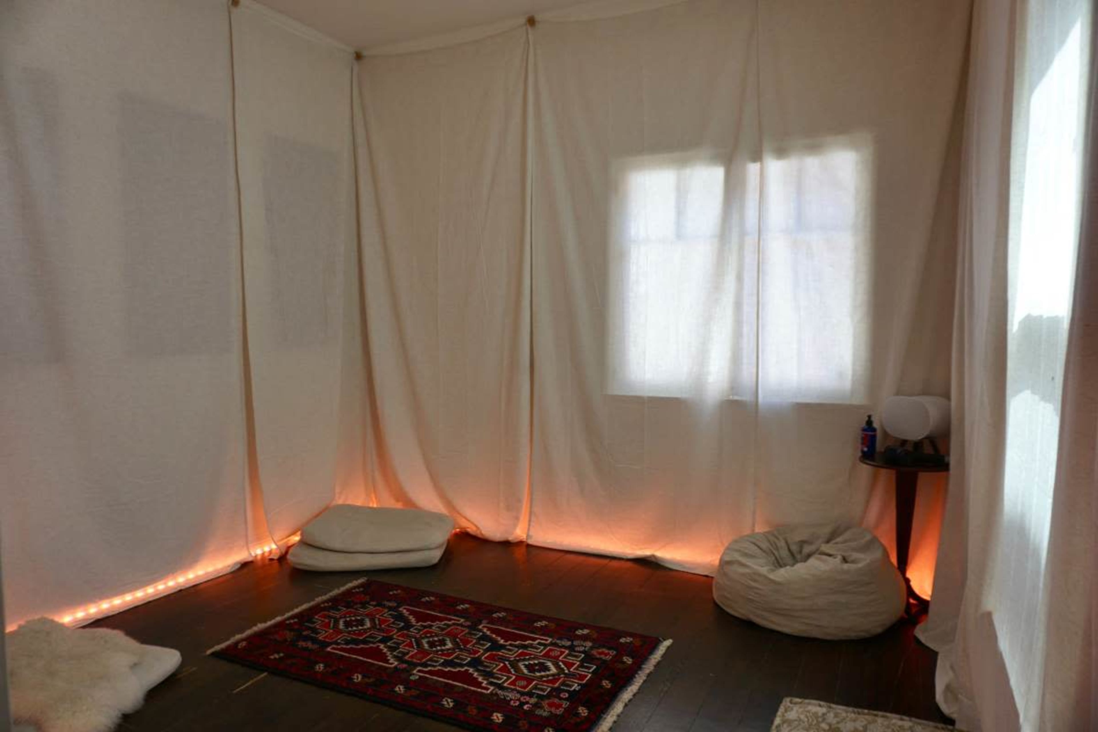 The room features soft floor seating, a decorative rug, and fabric draped along the walls, with ambient lighting along the base.